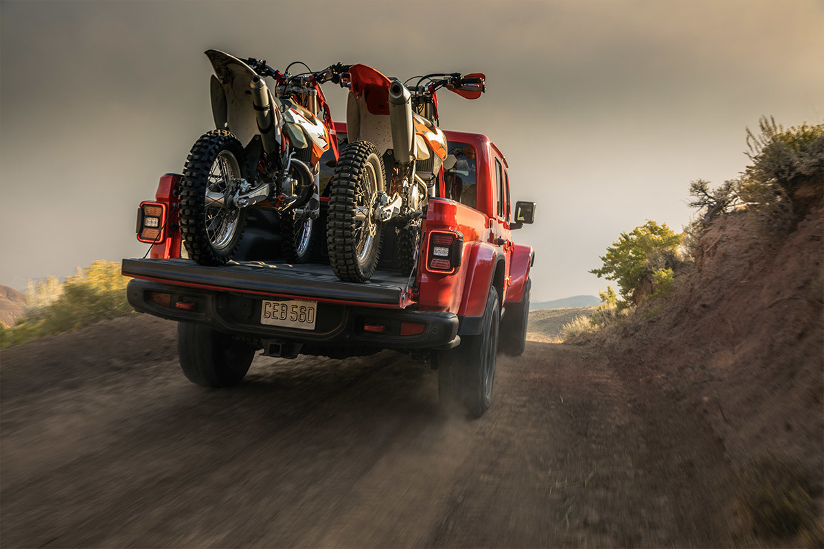 A 2022 Gladiator Rubicon in red parked on dirt patch with two dirt bikes in the truck bed.