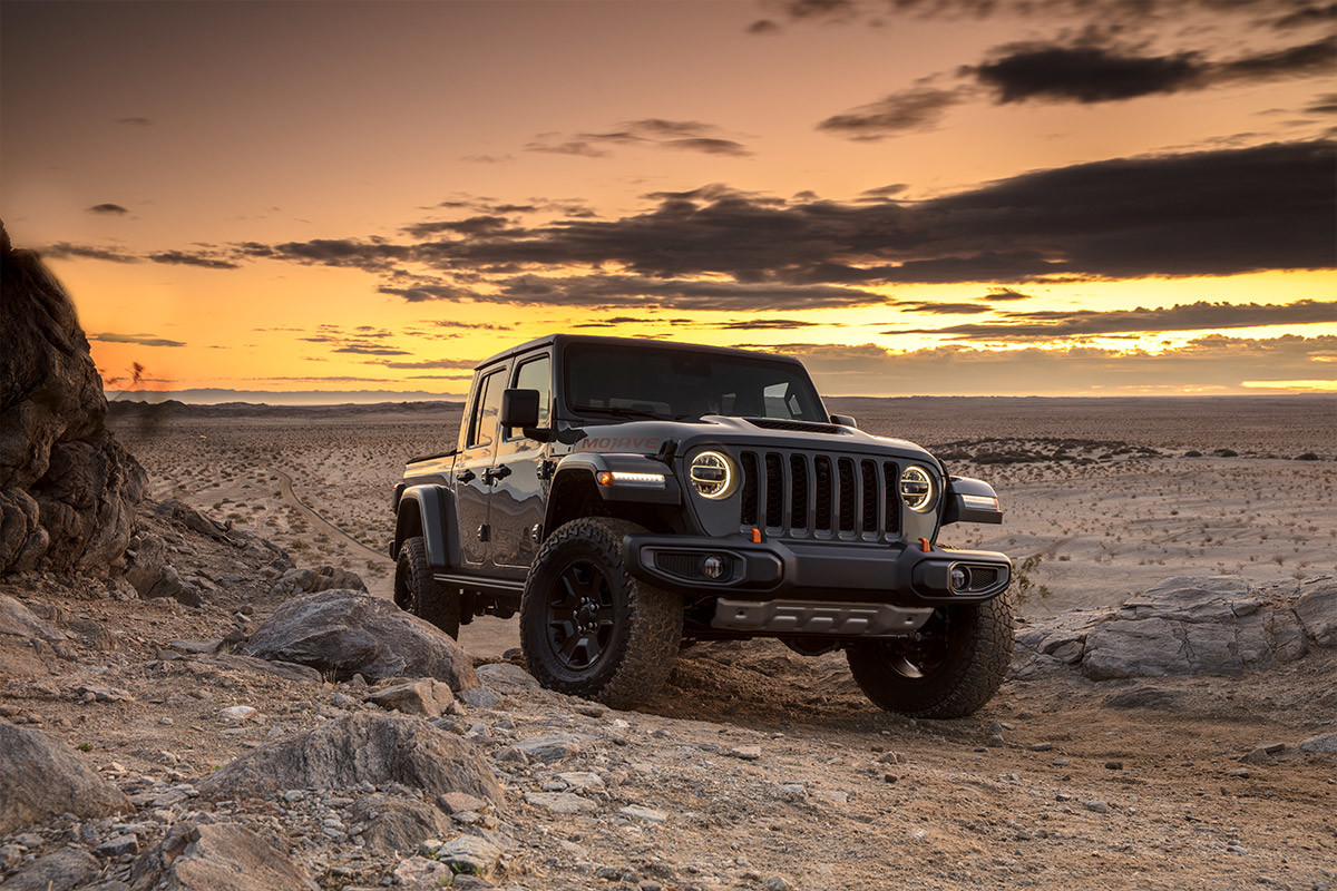 Black Jeep Gladiator Mojave parked in a vast desert landscape as the sun sets in the background.