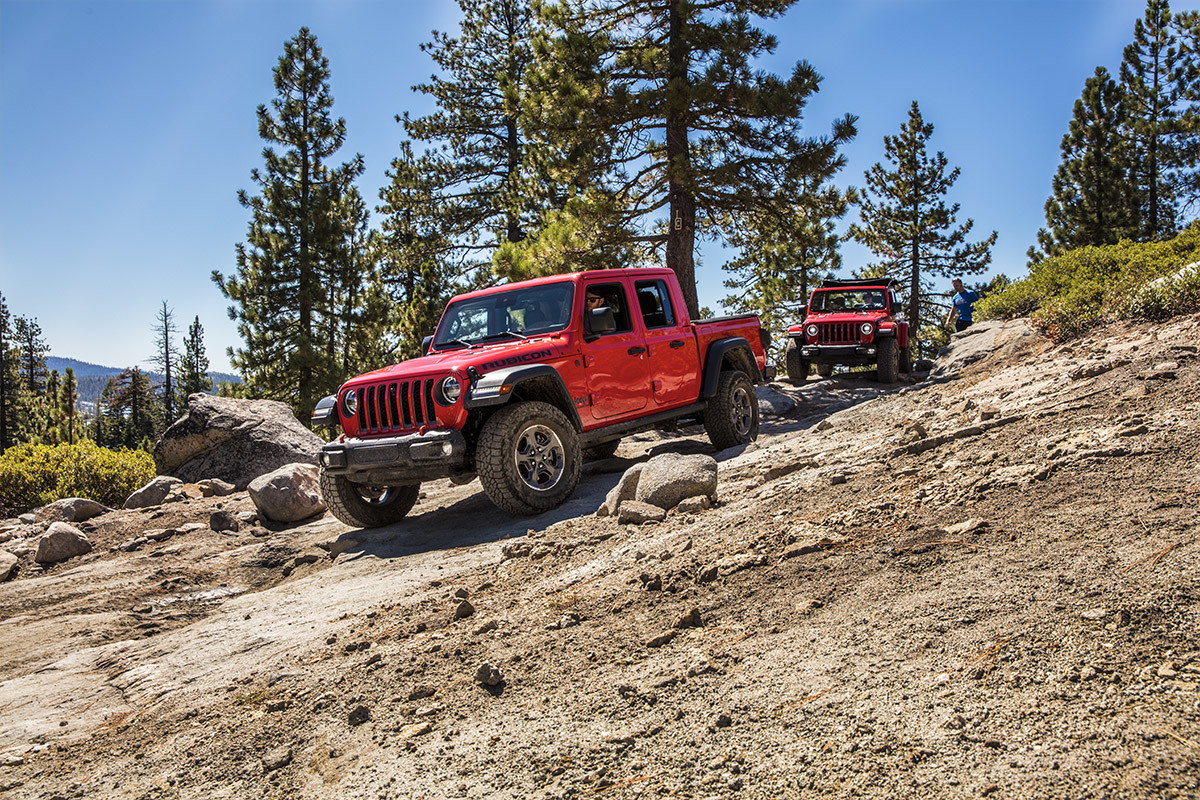 Two red Jeep Gladiator Rubicon vehicles driving one after another down a rocky off-road trail.