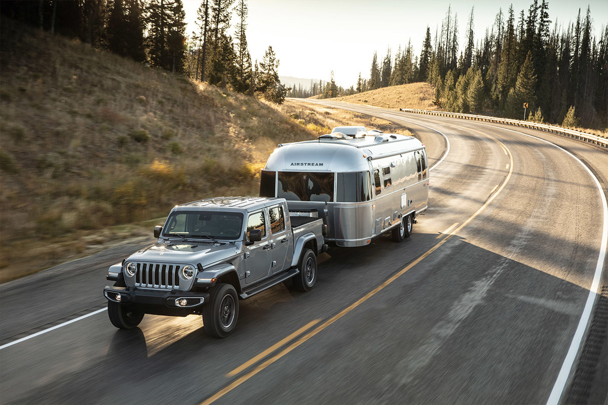 A gray 2022 Jeep Gladiator towing a camping trailer along the edge of a grassy field.