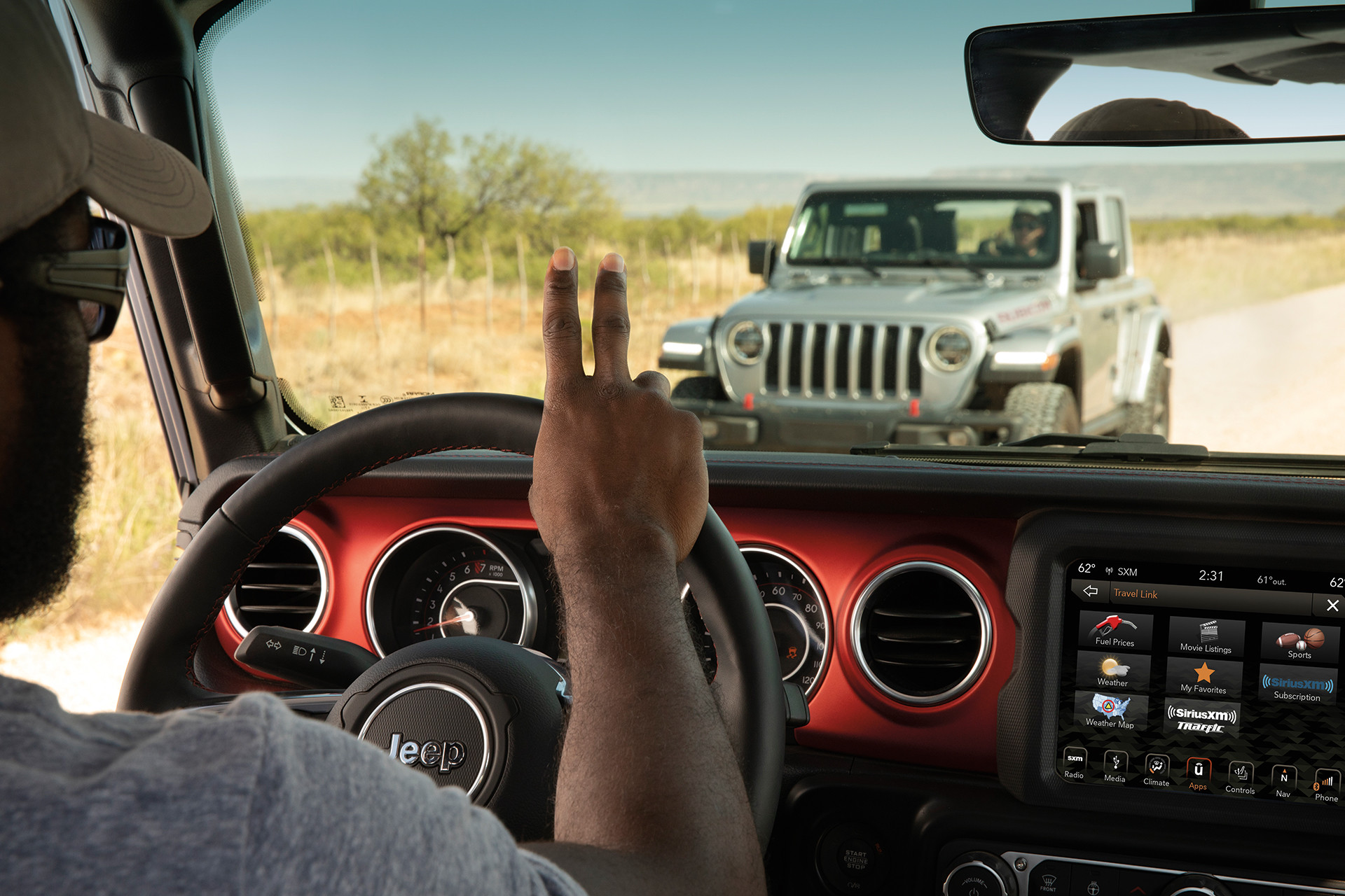 Interior view of a person giving a peace sign driving a 2022 Jeep Gladiator as they drive by another Jeep.