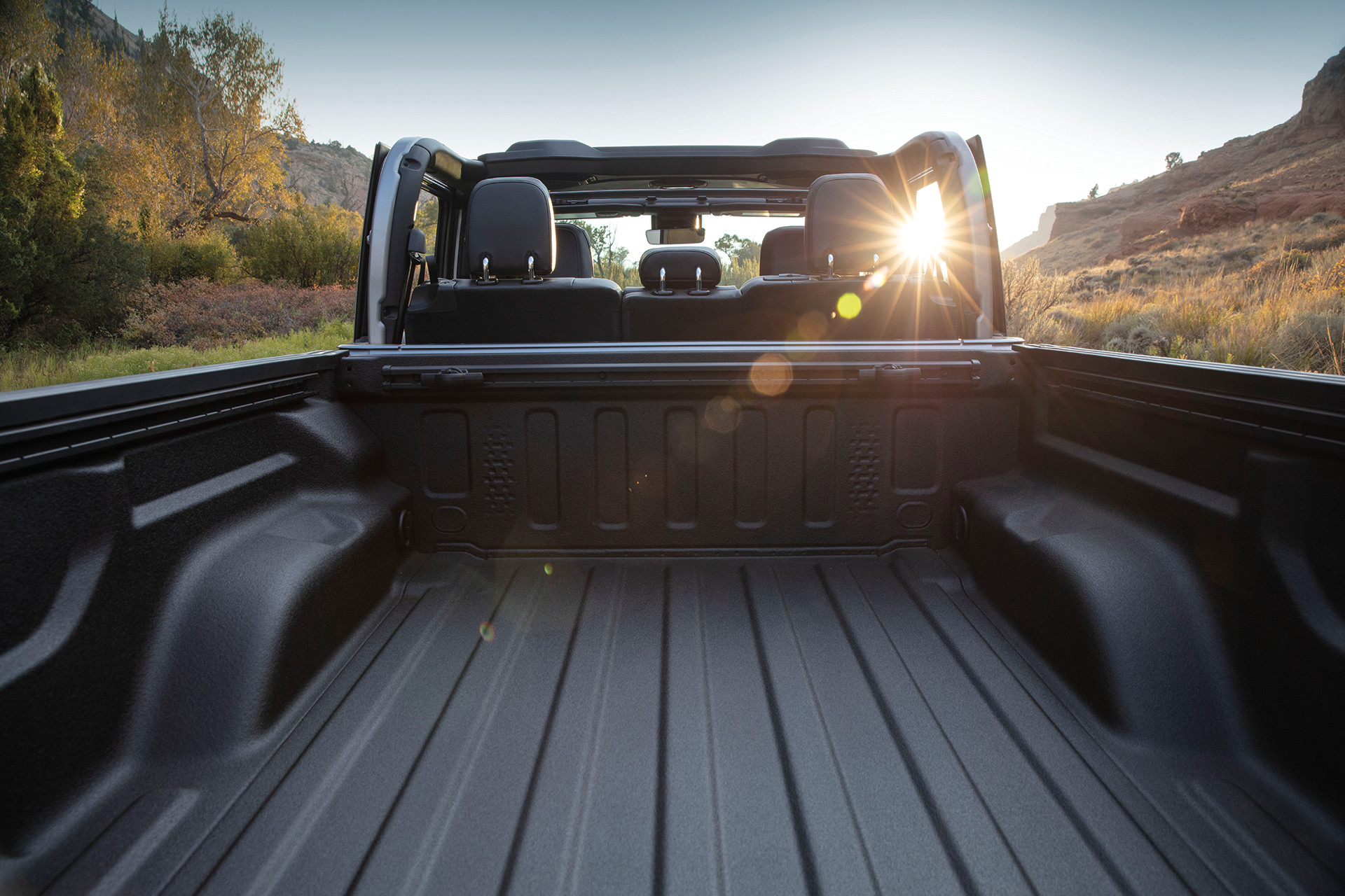 2022 Gladiator Rubicon in Silver Zynith featuring cargo bed, close up, with mountains and sunburst visible through passenger side window.