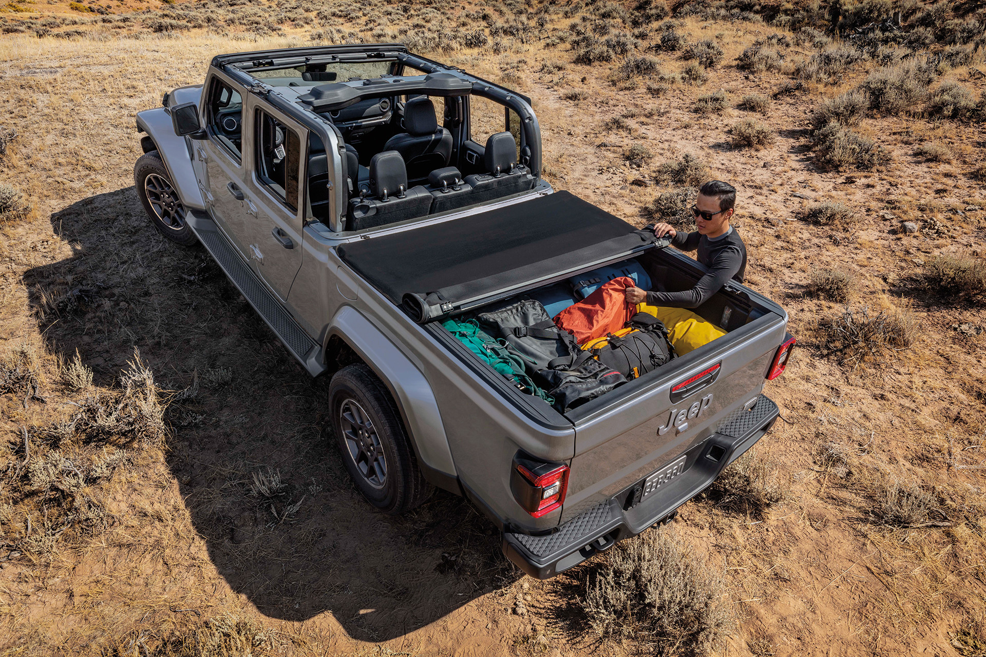Top down view of a dark grey 2022 Jeep gladiator with the truck bed filled with camping supplies and tonneau cover half on.