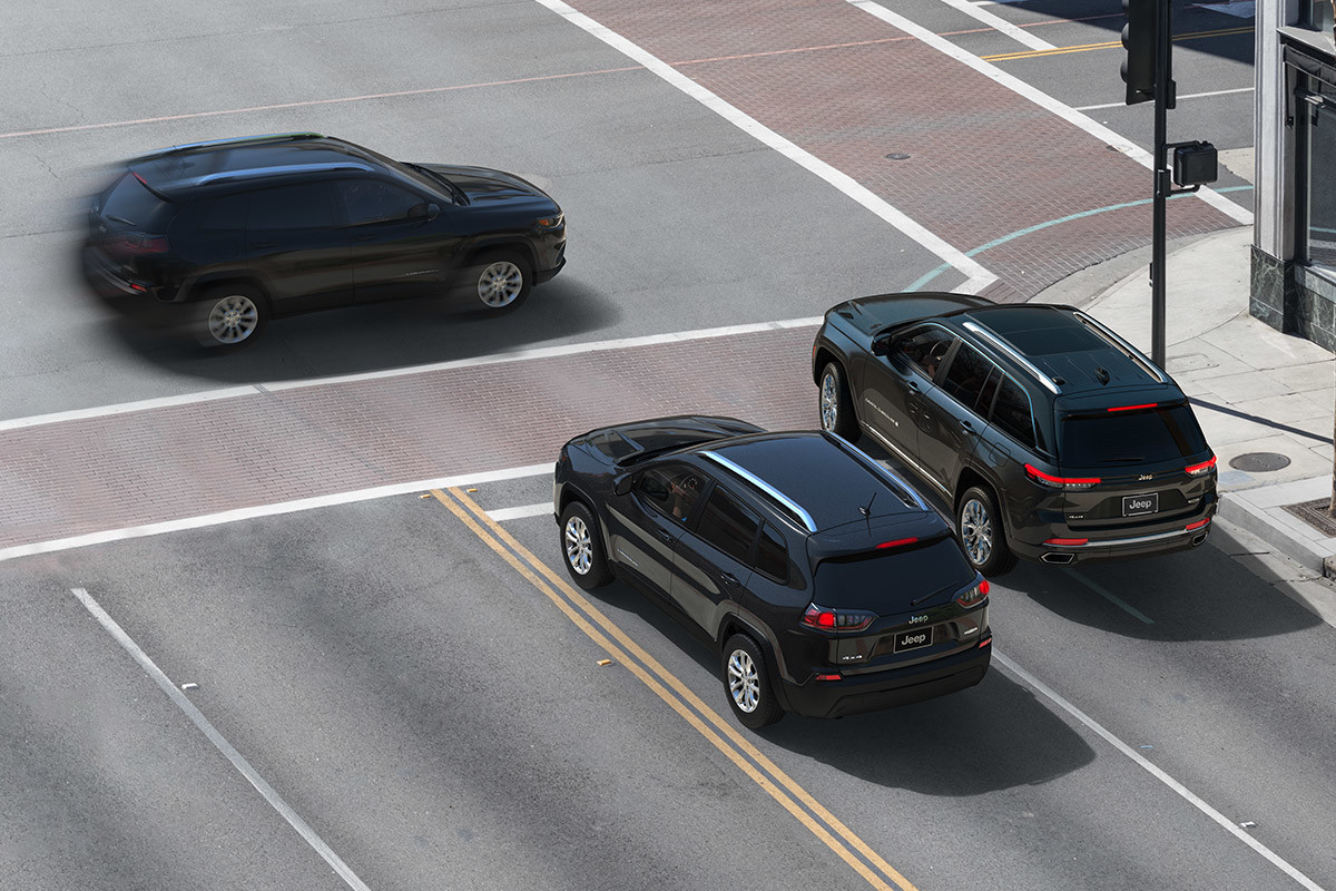 Nouveau système de prévention des collisions dans les <span class="unbr">intersections<fca-legal-tooltip label="*" key="*" type="disclaimer" ng-cloak>Ce système agit uniquement comme avertisseur, surveille uniquement l’avant du véhicule et n’intervient aucunement pour changer la dynamique du véhicule dans le but d’éviter une collision. Il ne remplace ni la vigilance, ni les interventions du conducteur. Le conducteur doit en tout temps surveiller la circulation et être prêt à freiner pour éviter toute collision.</fca-legal-tooltip></span> Deux Jeep Grand Cherokee 2022, un noir et un gris, immobiles à une intersection, tandis qu’un troisième Jeep Grand Cherokee 2022 traverse l’intersection.