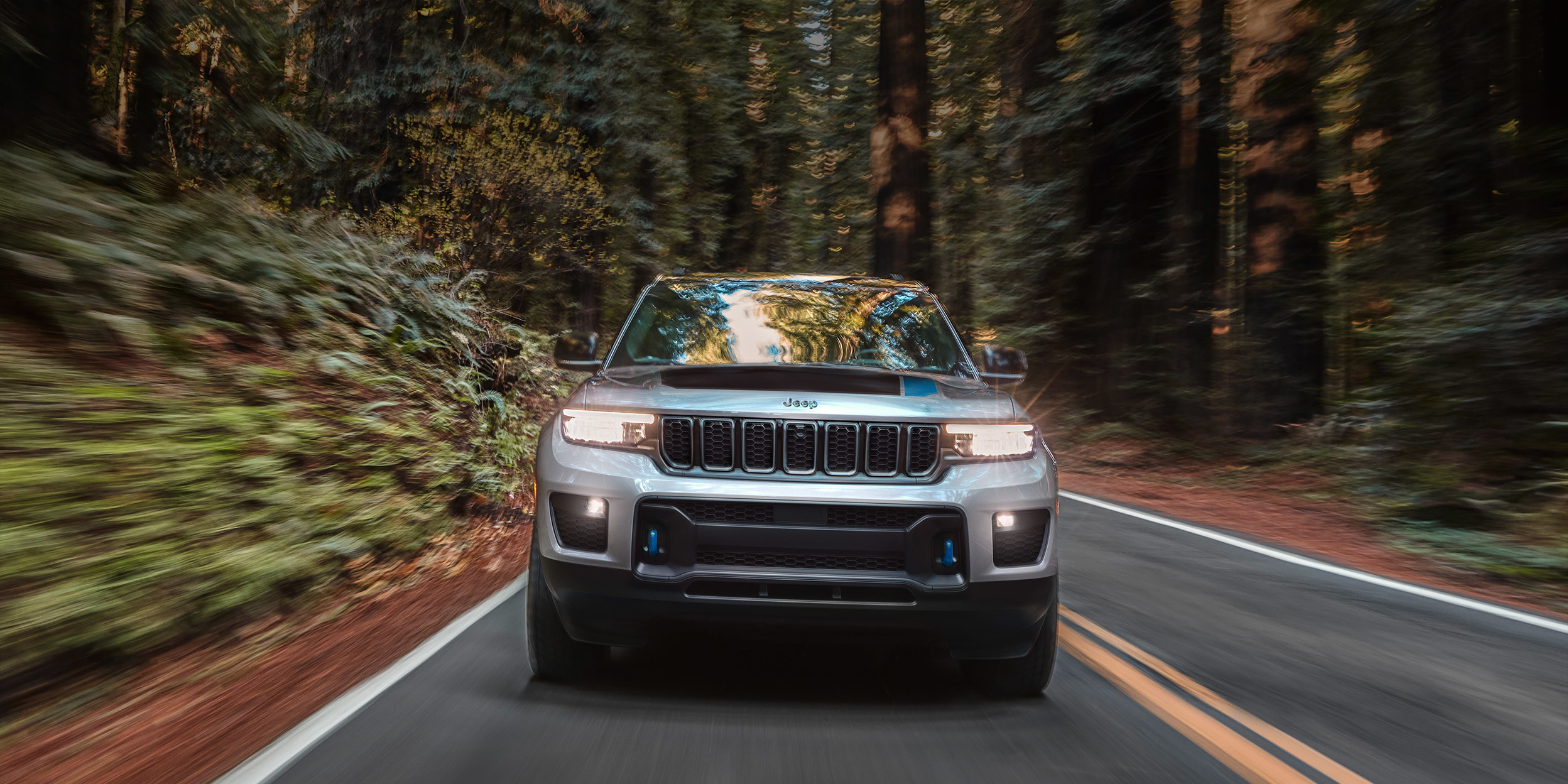 Jeep Grand Cherokee 2022 gris roulant sur une route pavée dans une forêt.