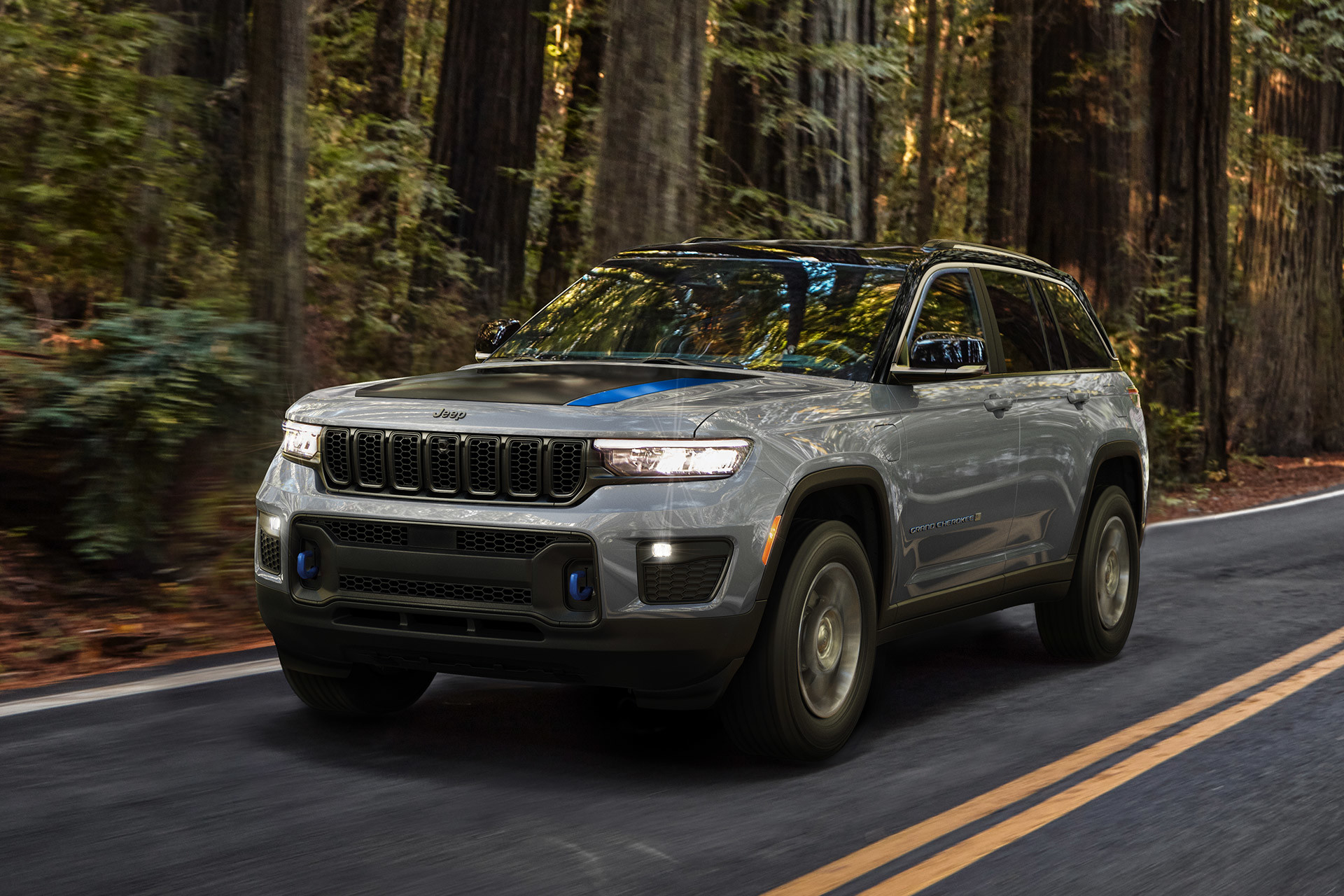 A grey 2022 Jeep Grand Cherokee being driven on a paved road through a forest.