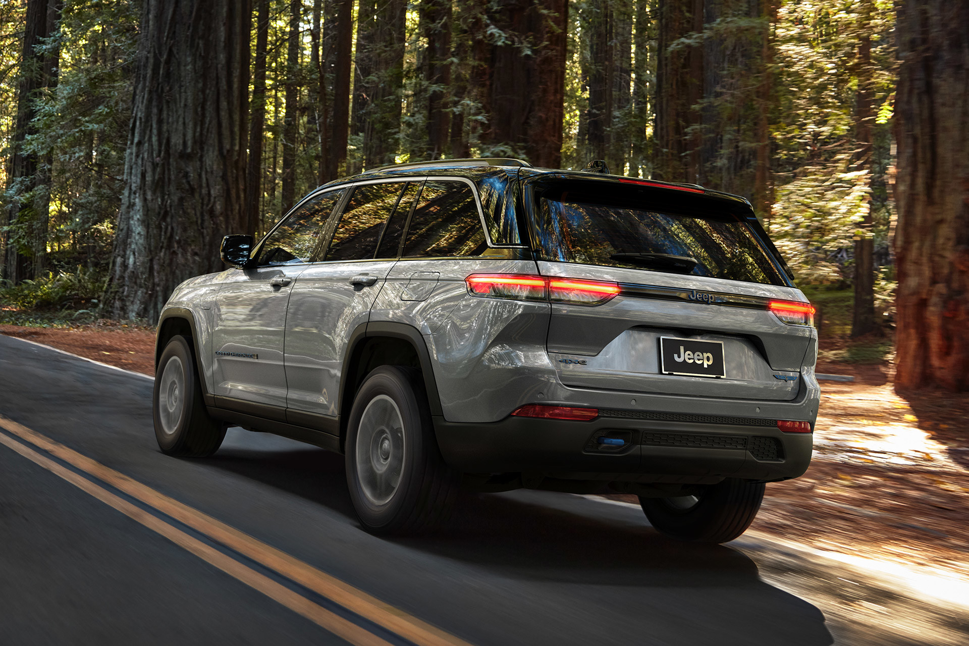 A grey 2022 Jeep Grand Cherokee being driven on a paved road through a forest.