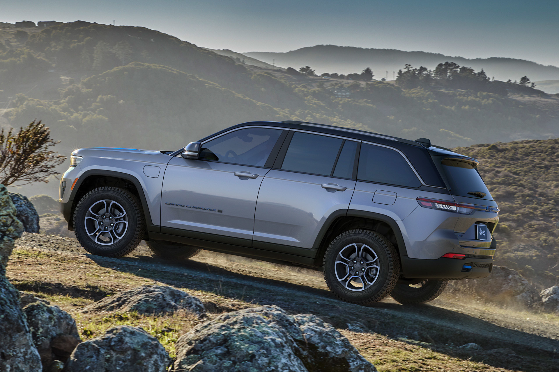 A grey 2022 Jeep Grand Cherokee being driven up a rocky hill with mountains in the background.