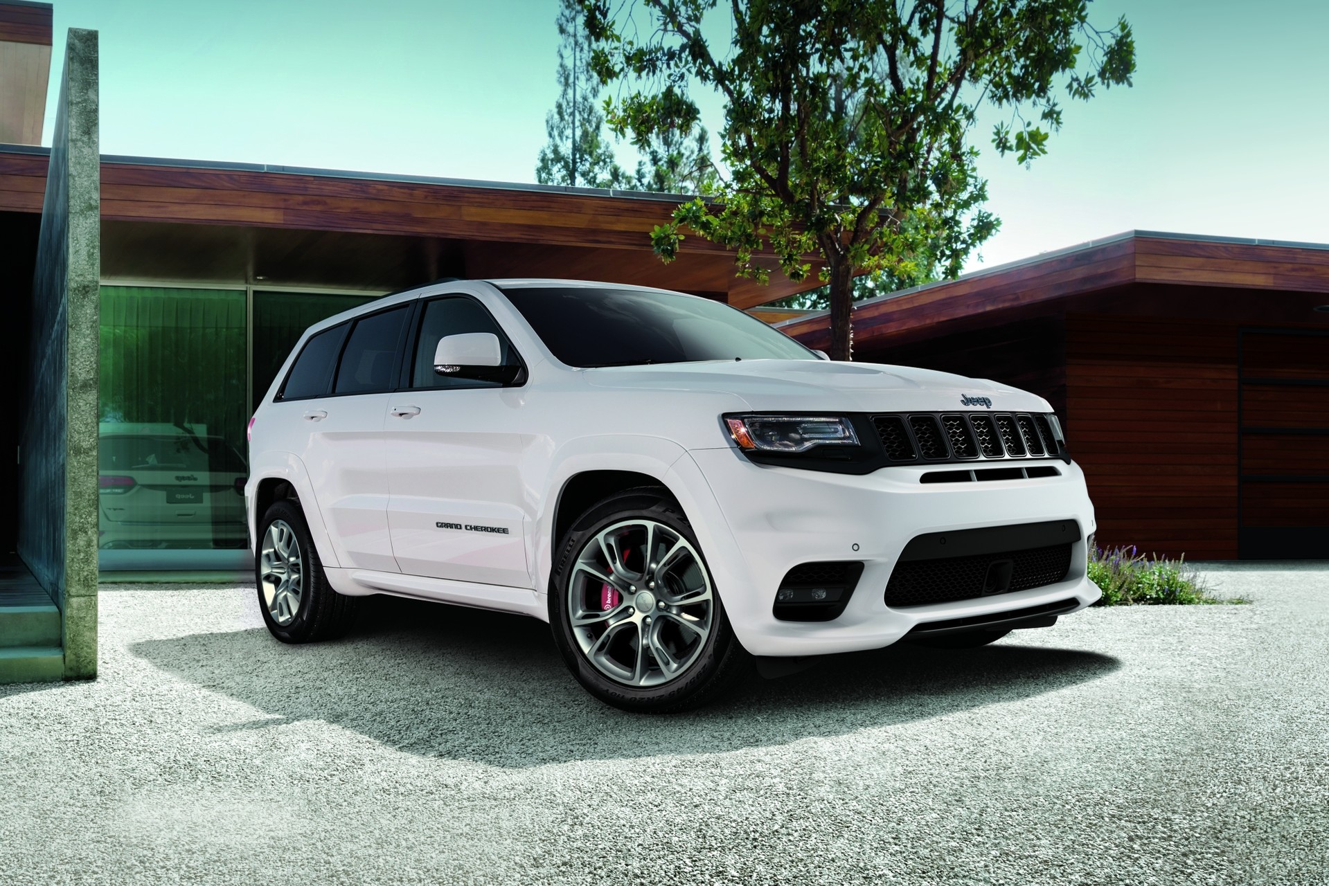 White 2020 Jeep Grand Cherokee driving through a forested area on a road.