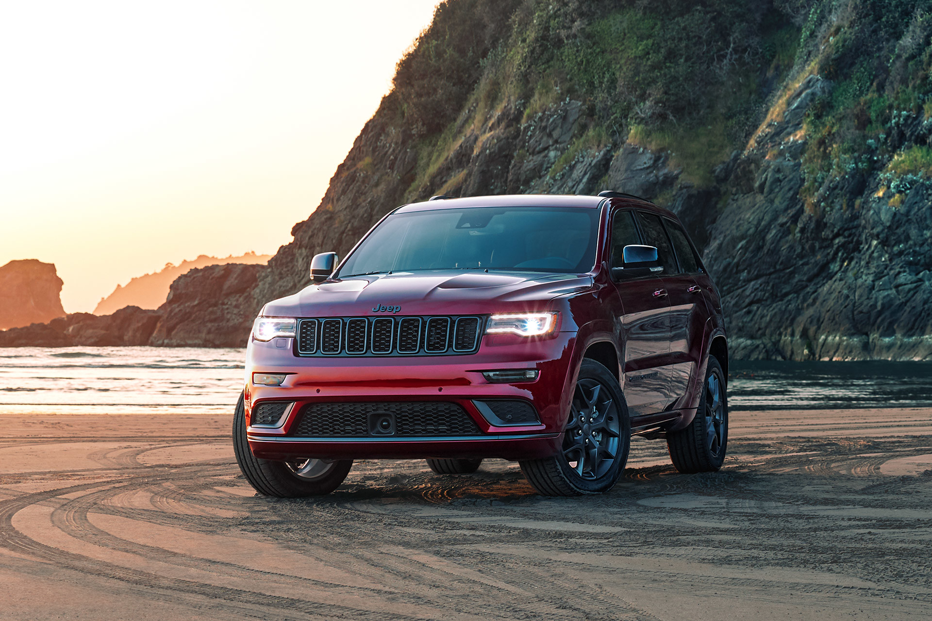 Jeep Grand Cherokee rouge 2020 stationné sur la plage avec des montagnes.
