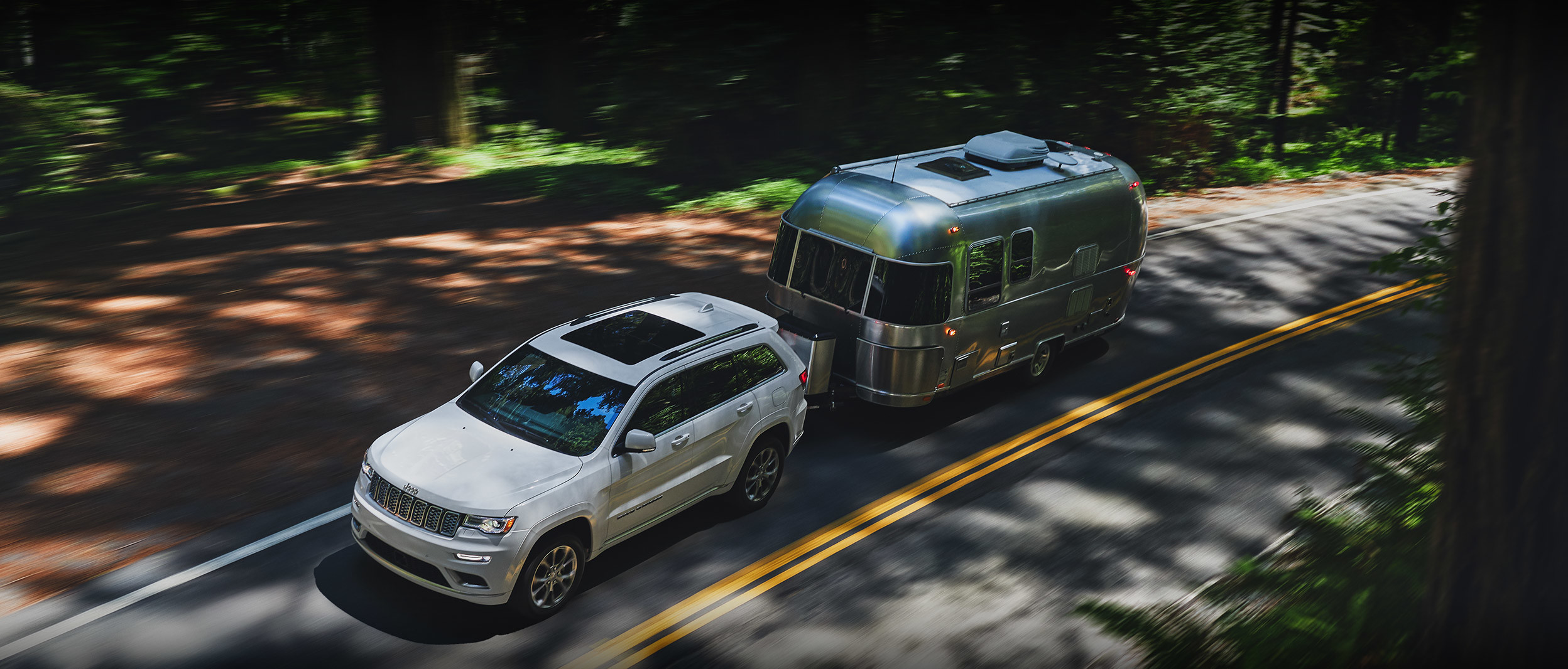 White 2020 Jeep Grand Cherokee towing a large silver RV.