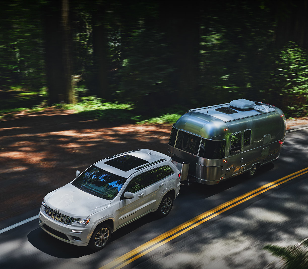 White 2020 Jeep Grand Cherokee towing a large silver RV.