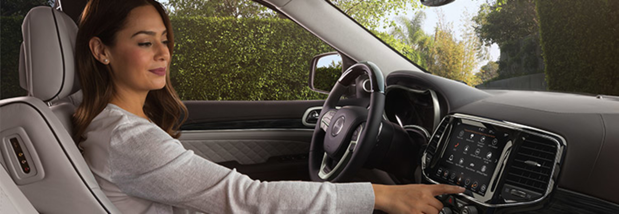 Femme occupant le siège du conducteur d’un Jeep Grand Cherokee et utilisant l’écran tactile du centre multimédia Uconnect.
