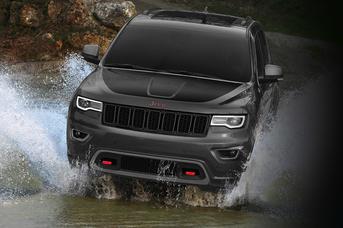 Grey Jeep Grand Cherokee making a splash while driving into a large puddle.
