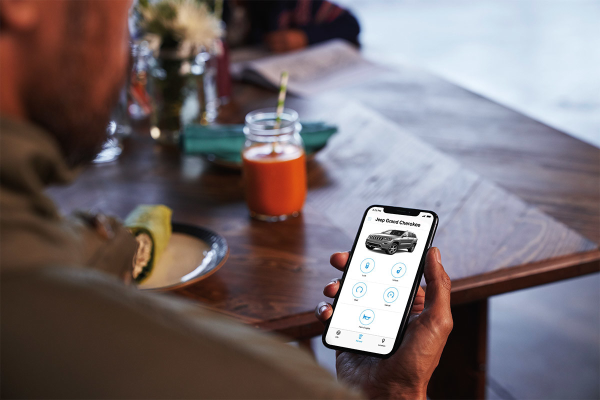 Homme tenant un téléphone intelligent et montrant les options du service SiriusXM Guardian pour verrouiller ou déverrouiller le Jeep Grand Cherokee à distance.