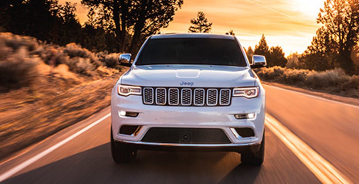 MOST AWARDED SUV EVER<fca-legal-tooltip label="*" key="*" type="disclaimer" ng-cloak>Jeep<sub>®</sub> Grand Cherokee has received more awards over its lifetime than any other SUV.</fca-legal-tooltip> Front view of a white 2021 Grand Cherokee Summit being driven on a road at sunset