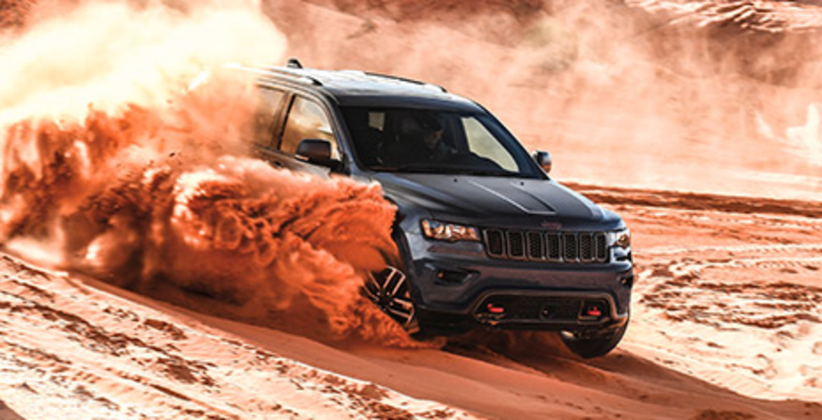 MOST CAPABLE SUV IN ITS CLASS<fca-legal-tooltip label="*" key="*" type="disclaimer" ng-cloak>Based on WardsAuto Middle Sport/Utility segmentation. When properly equipped.</fca-legal-tooltip> Front quarter view of a black 2021 Grand Cherokee being driven in the sand