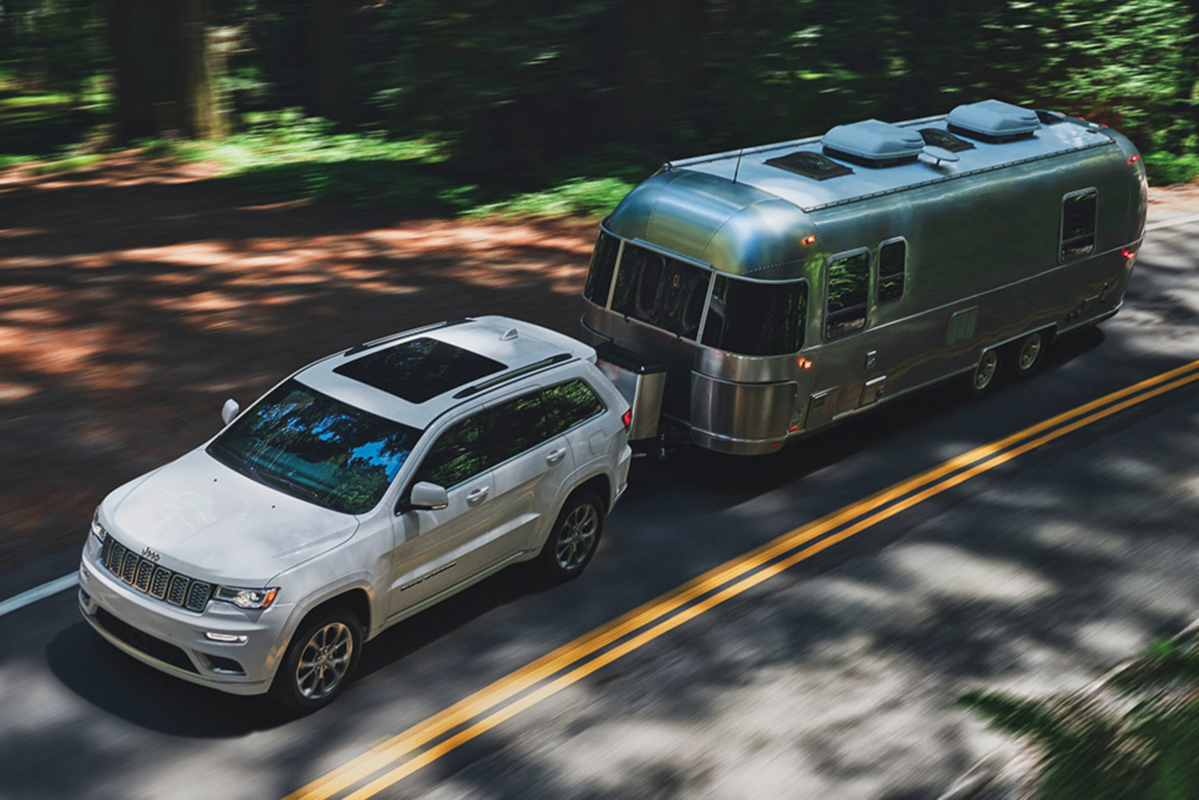 Overhead view of a black Grand Cherokee towing a boat on a road next to a river