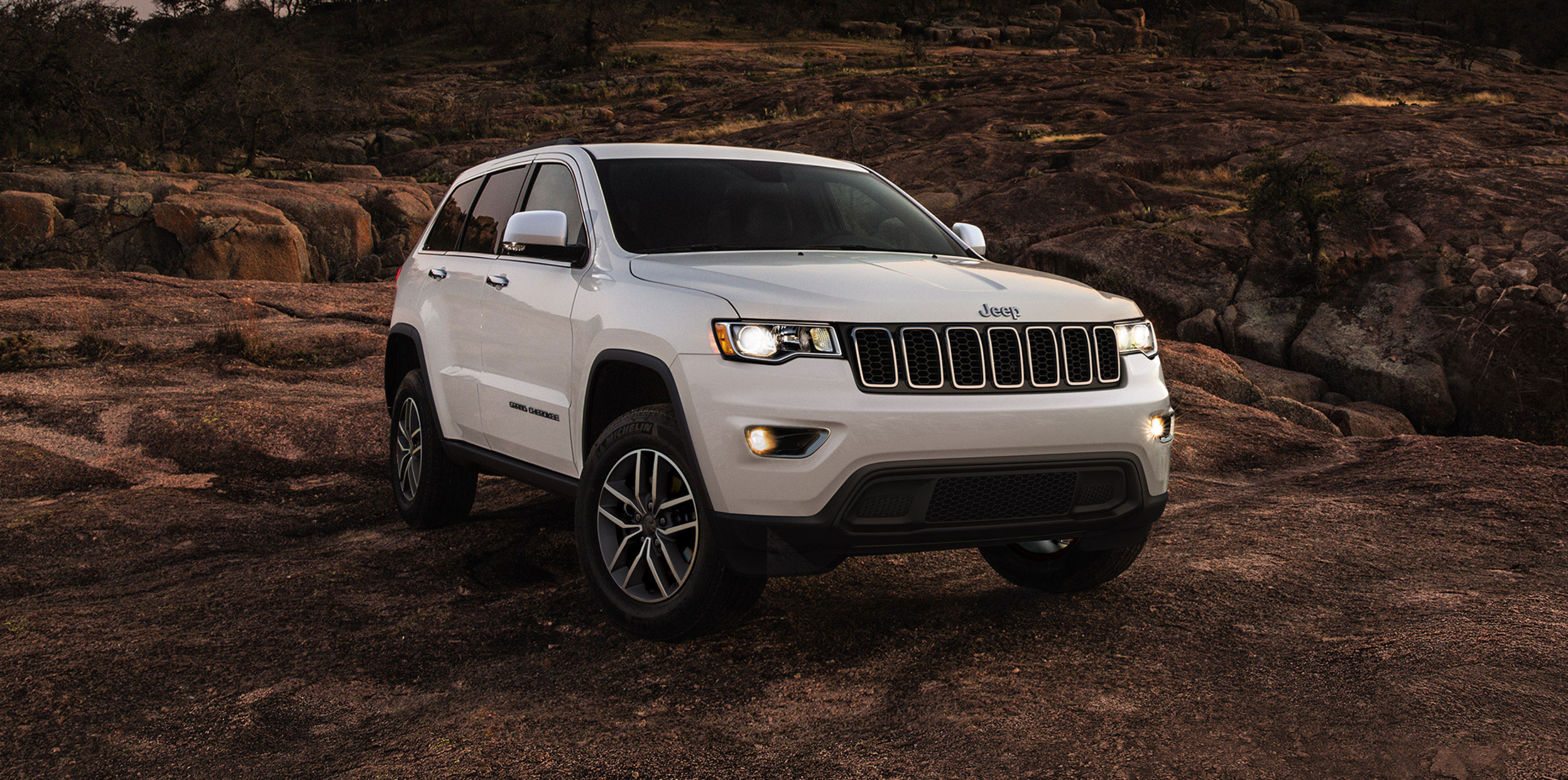 2021 Grand Cherokee Laredo in Bright White parked on a rocky cliff with lights on