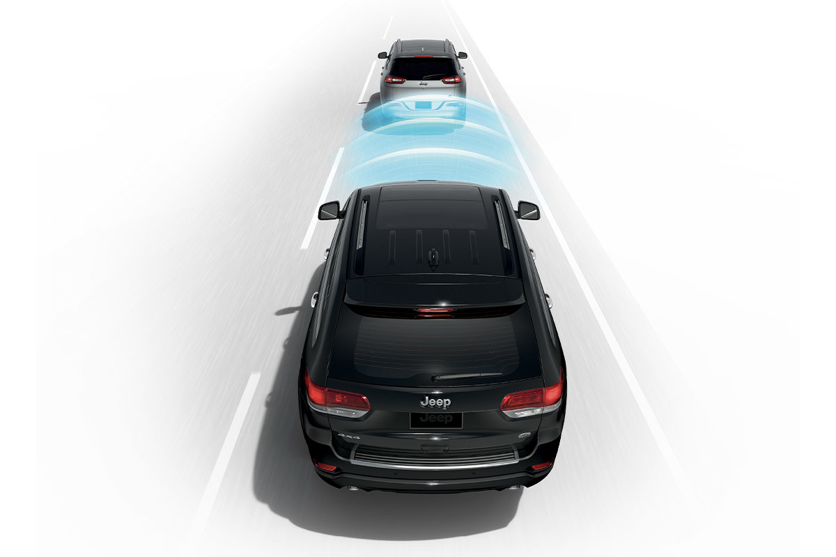 Vue arrière du Grand Cherokee WK en mouvement derrière un autre véhicule, montrant la fonction d’alerte de collision avant et les capteurs de freinage actif.