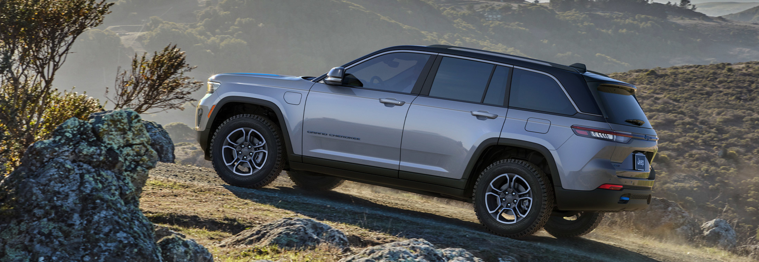 A grey All-New 2022 Jeep Grand Cherokee 4xe being driven off road, up a hill.