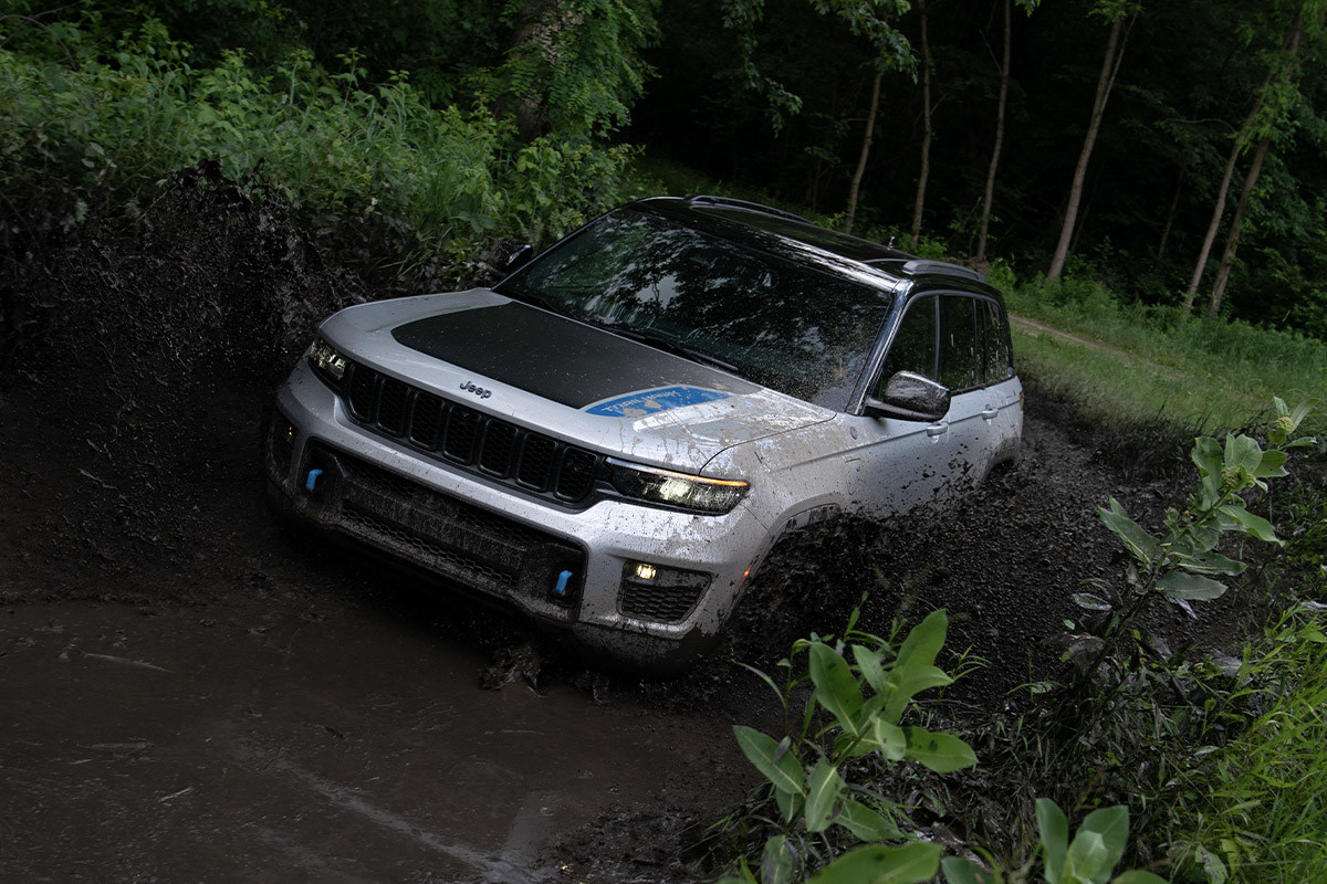 Vue avant d’un tout nouveau Jeep Grand Cherokee 4xe 2022 argent roulant dans la boue.