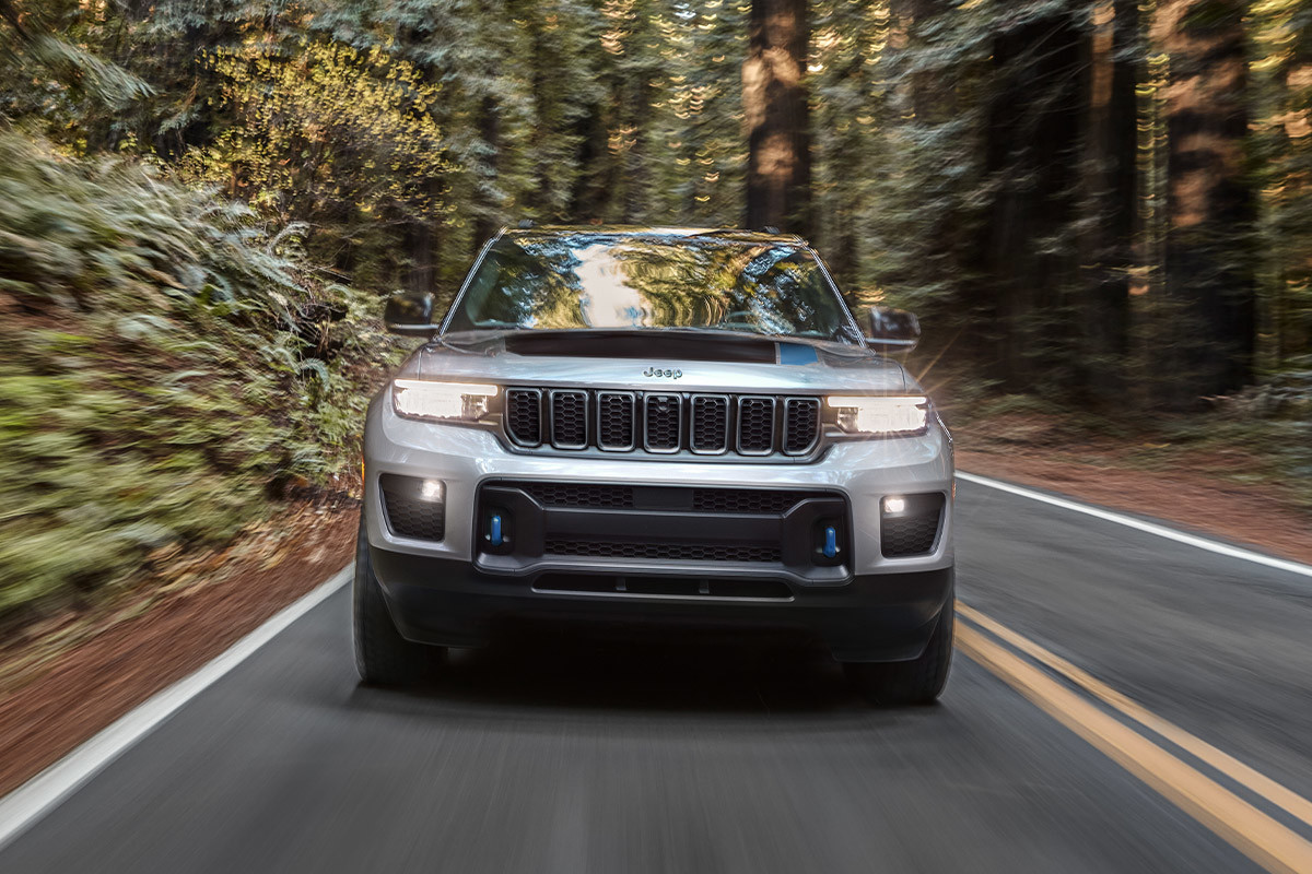 The front of a white All-New 2022 Jeep Grand Cherokee 4xe being driven through the woods.