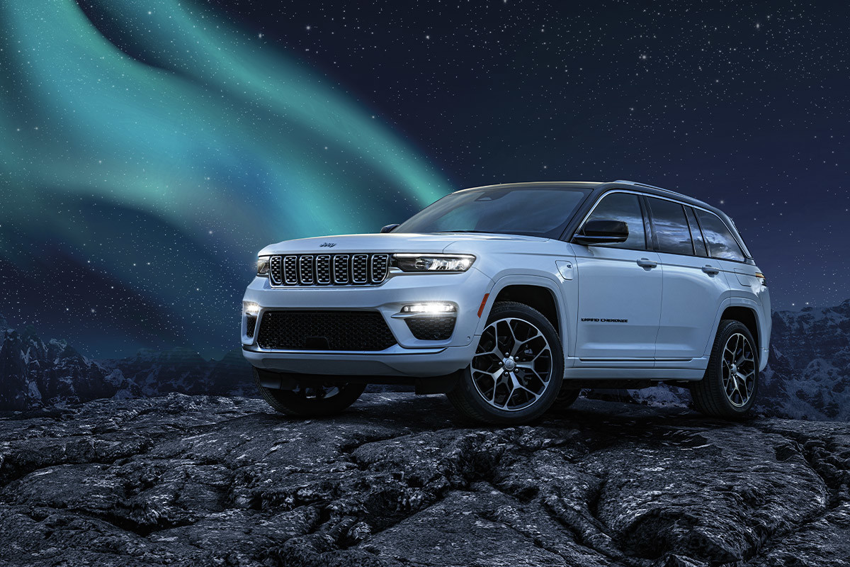 A white All-New 2022 Jeep Grand Cherokee 4xe parked on a rocky terrain with the northern lights visible in the background.