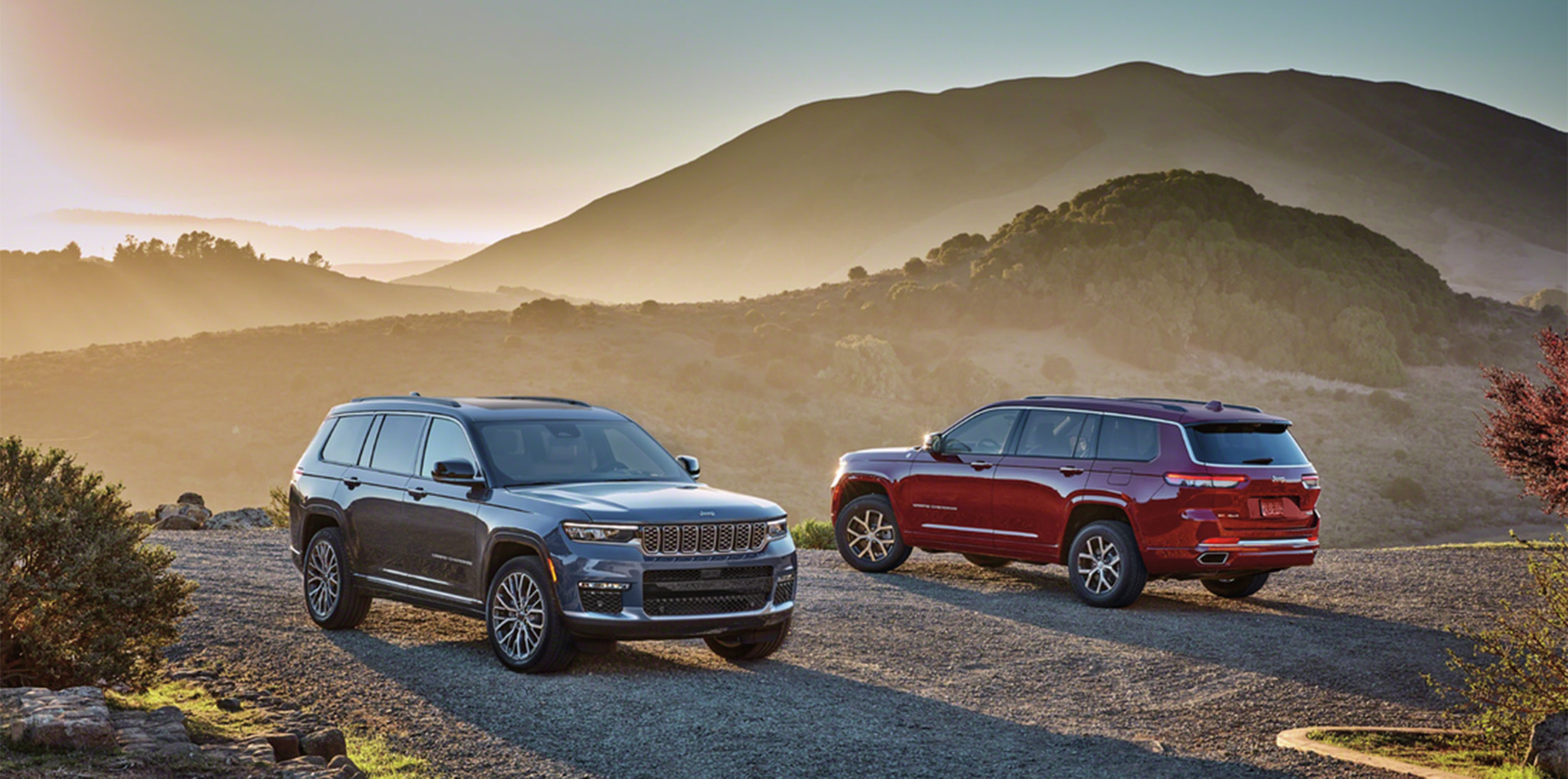 Jeep Grand Cherokee noir et un Jeep Grand Cherokee rouge garés avec des montagnes en arrière-plan.