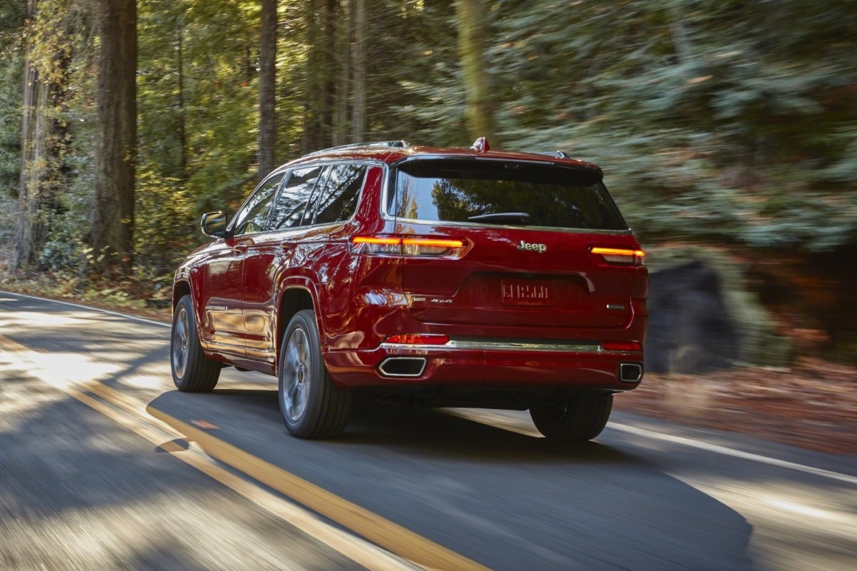 Vue arrière d'un Jeep Grand Cherokee L 2021 rouge roulant sur une autoroute à côté d'une forêt.