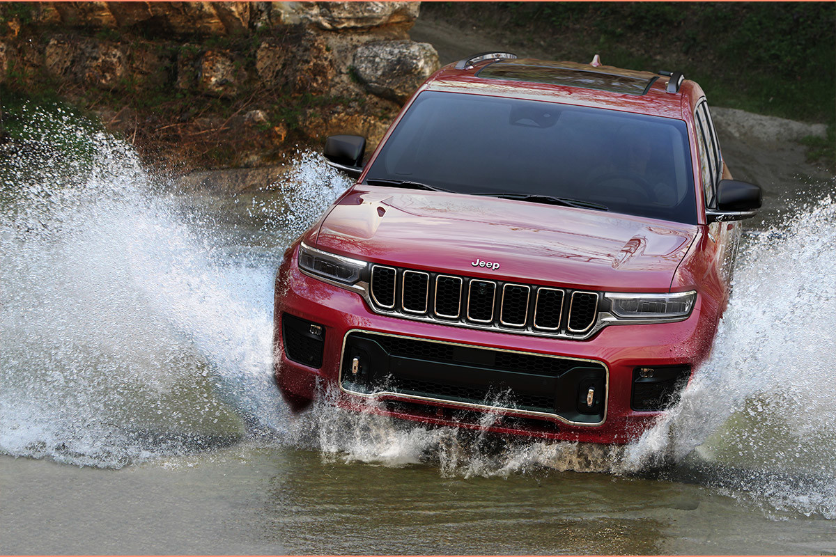 Vue de face du tout nouveau Grand Cherokee L 2021 rouge créant des éclaboussures d’eau en traversant une rivière.