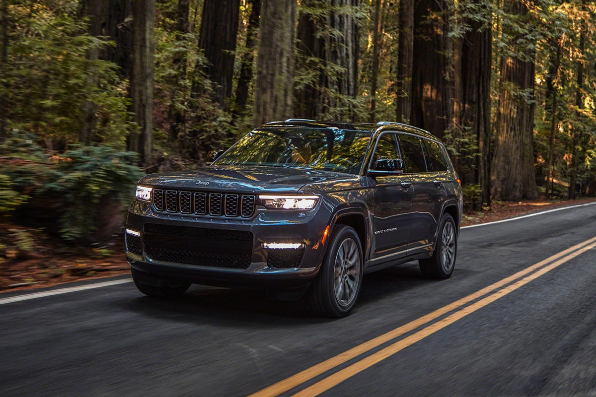 CONÇU POUR VOUS Tout nouveau Grand Cherokee L 2021 gris roulant sur une route pavée dans une forêt dense.