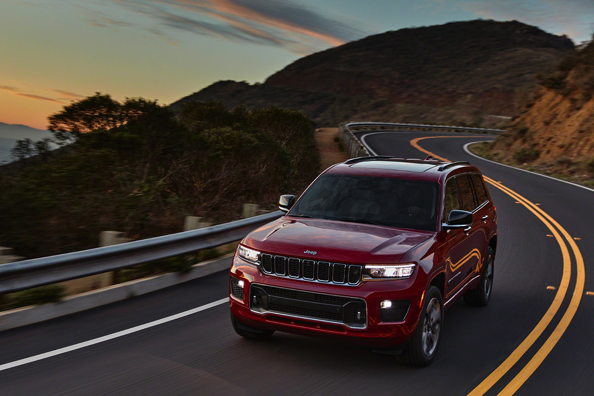 Vue avant d’un tout nouveau Grand Cherokee L 2021 rouge roulant sur une route de montagne sinueuse.