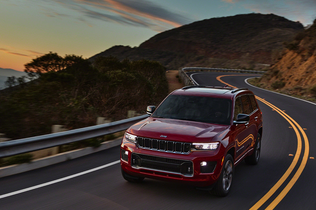 Vue avant d’un Grand Cherokee L rouge, les phares à DEL illuminant vivement une route montagneuse.