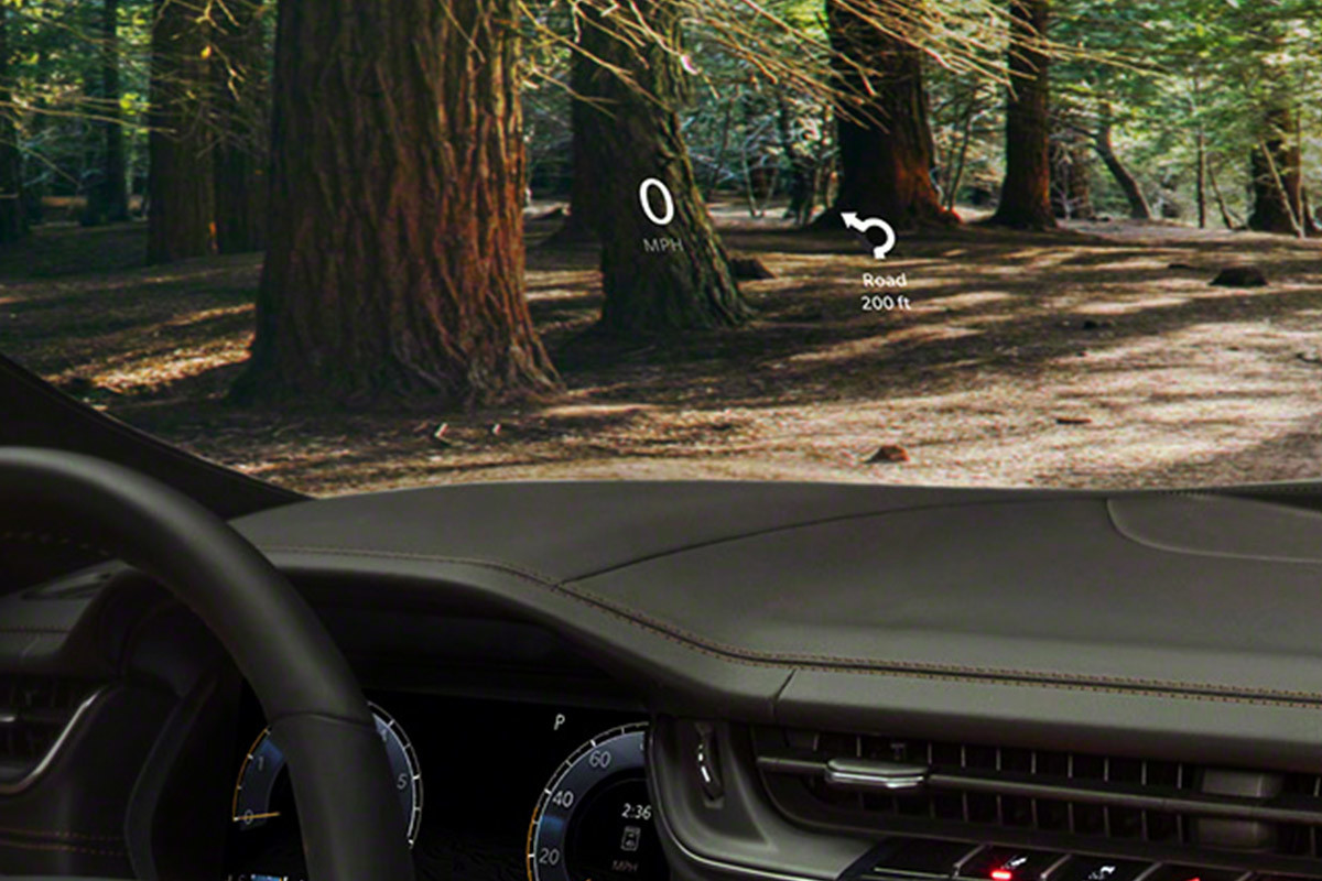 Gros plan des sièges avant en cuir Nappa, du volant et du centre multimédia Uconnect doté d’un écran tactile de 10,1 po à l’intérieur du Grand Cherokee L 2021. Des arbres illuminés par le soleil sont visibles à travers le pare-brise.