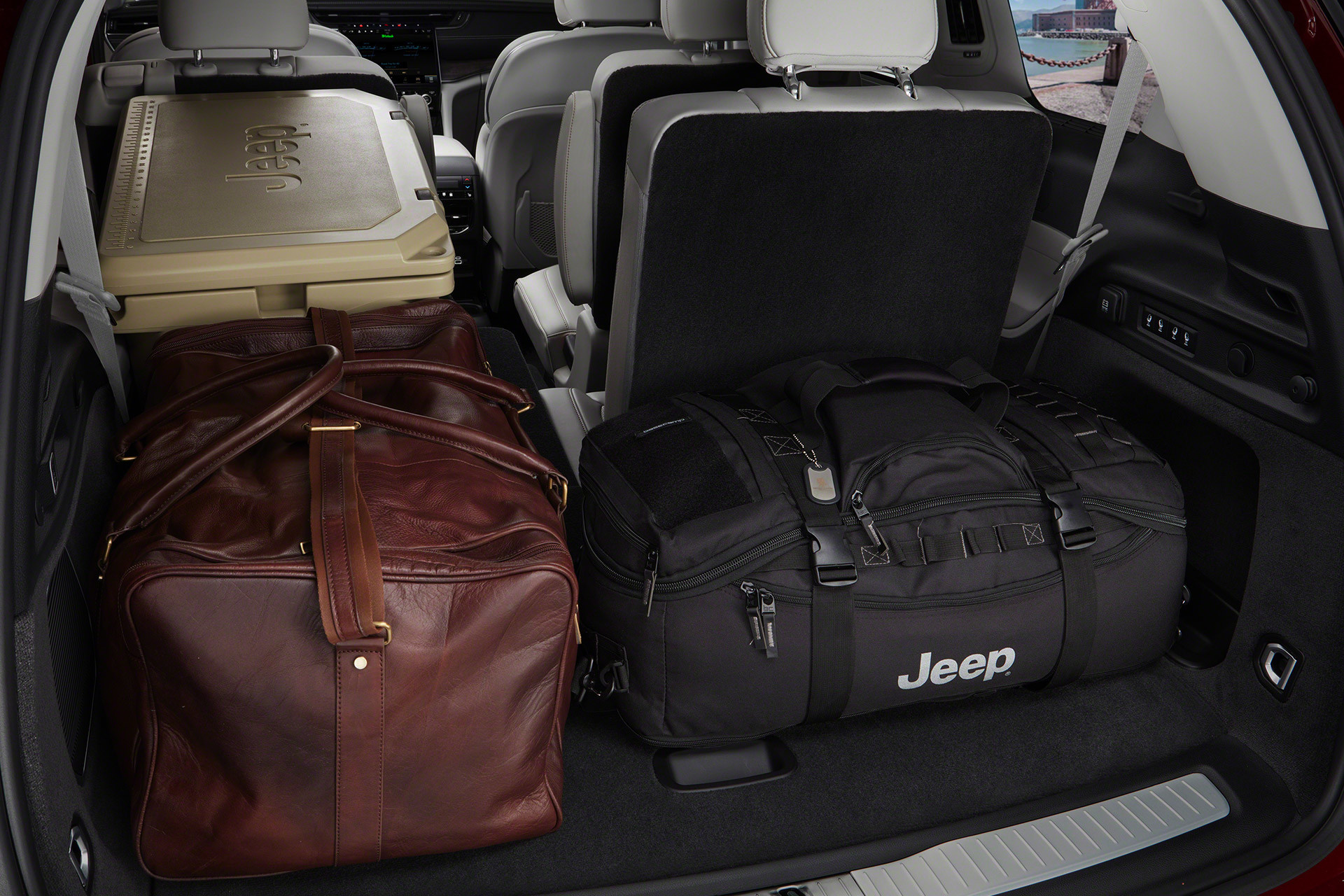 Gros plan de la partie arrière du tout nouveau Grand Cherokee L 2021, avec un des sièges de deuxième rangée et un des sièges de troisième rangée rabattus pour offrir de l’espace pour les bagages et un sac noir de la marque Jeep.