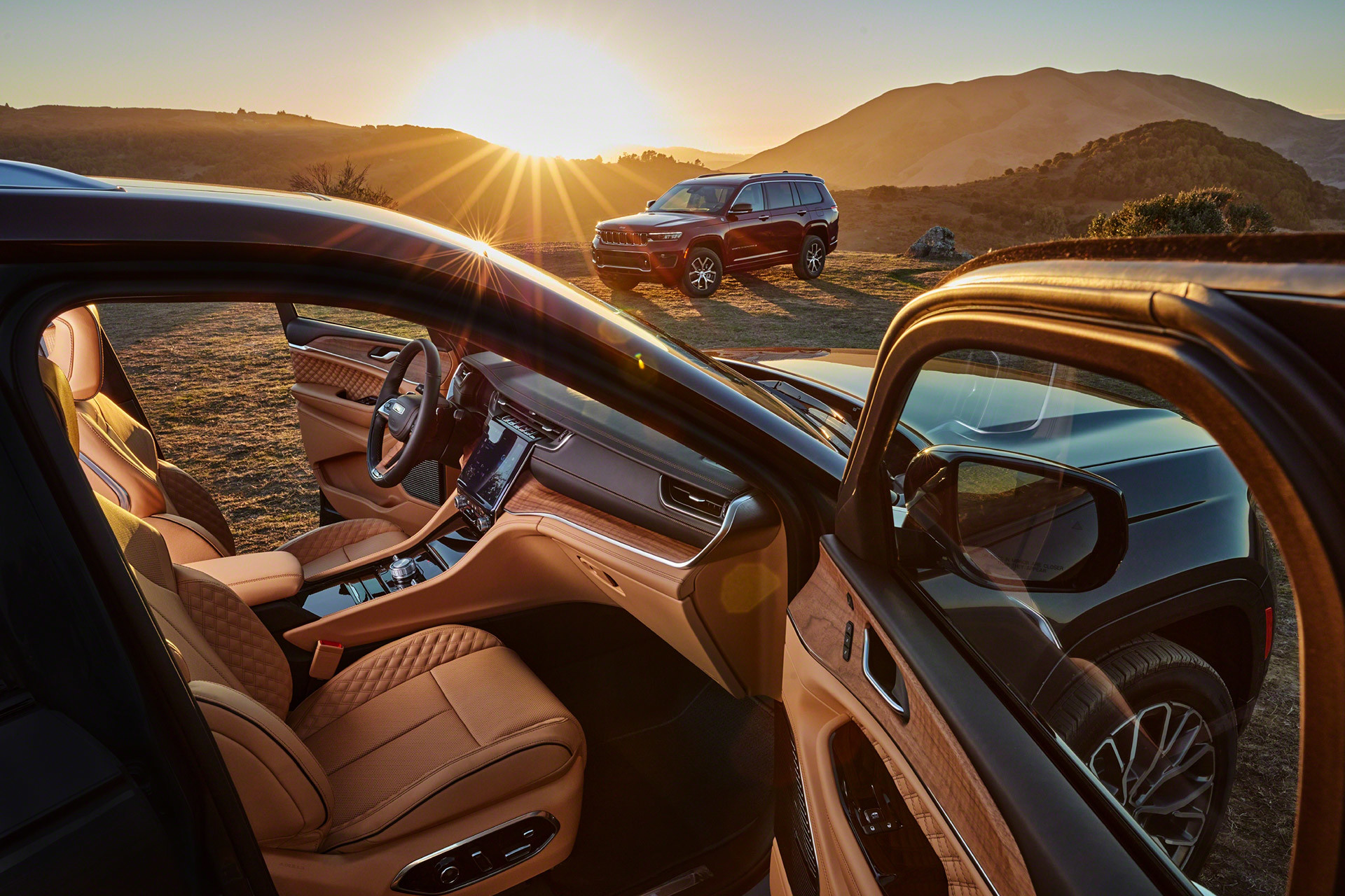 Gros plan du tout nouveau Grand Cherokee L 2021, la porte du passager avant ouverte pour révéler les sièges en cuir Nappa livrables en option et les commodités luxueuses. Un deuxième Grand Cherokee L est garé en arrière-plan, un soleil couchant au loin.