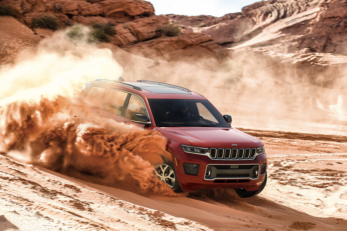 Un Jeep Grand Cherokee 2022 rouge soulevant un nuage de sable en descendant un banc de sable