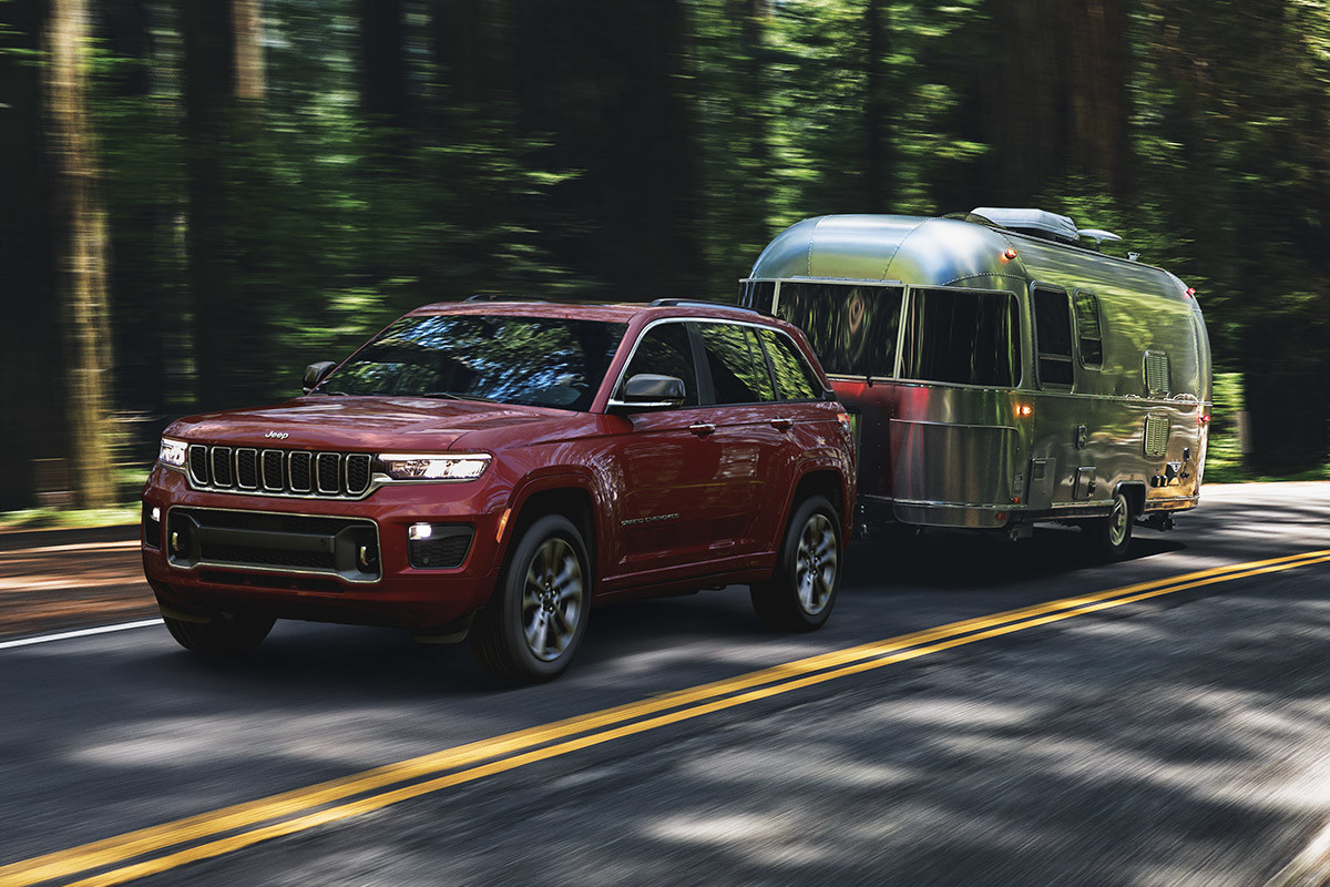Un Jeep Grand Cherokee 2022 rouge tractant une remorque argent dans la forêt
