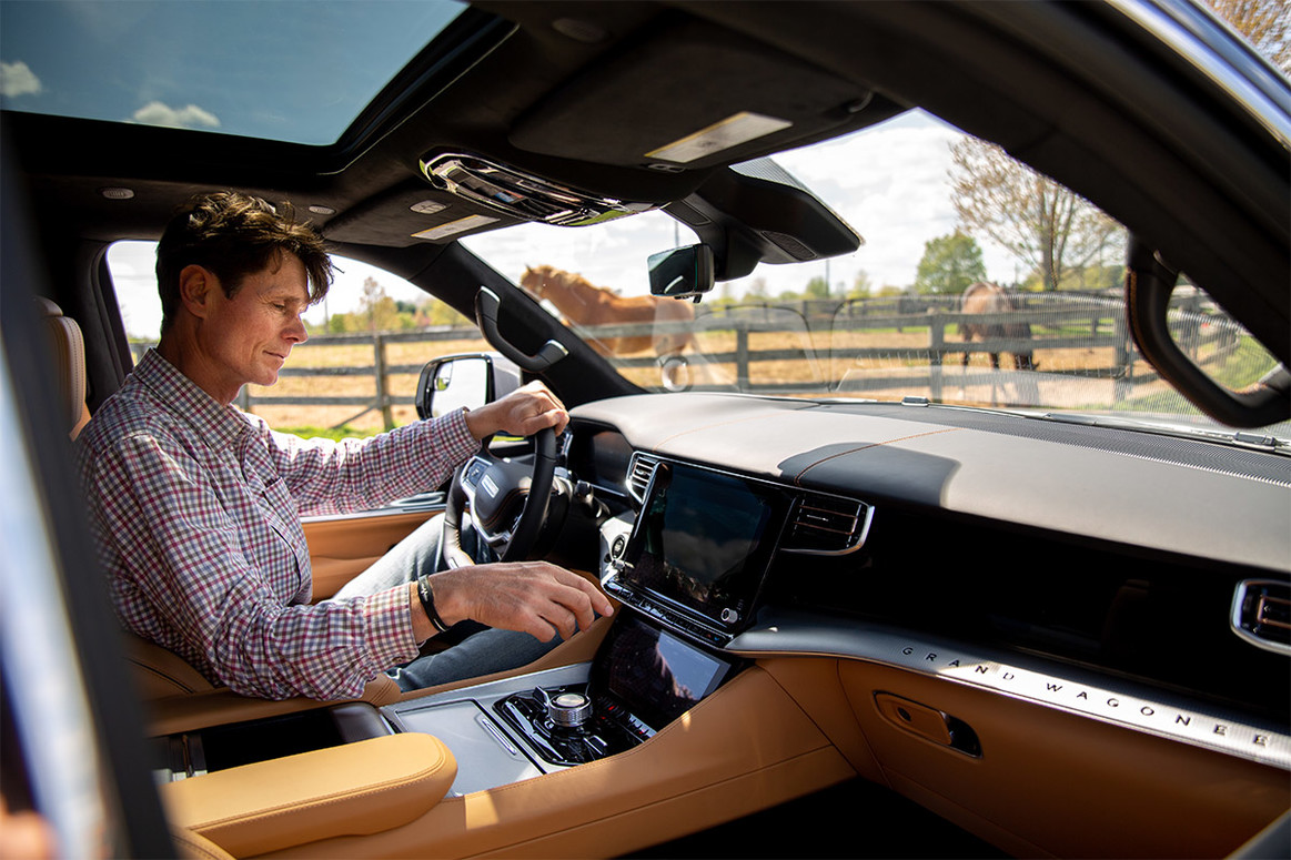 Vue côté passager d'une personne assise sur le siège conducteur interagissant avec le système UConnect du Jeep Grand Wagoneer 2022