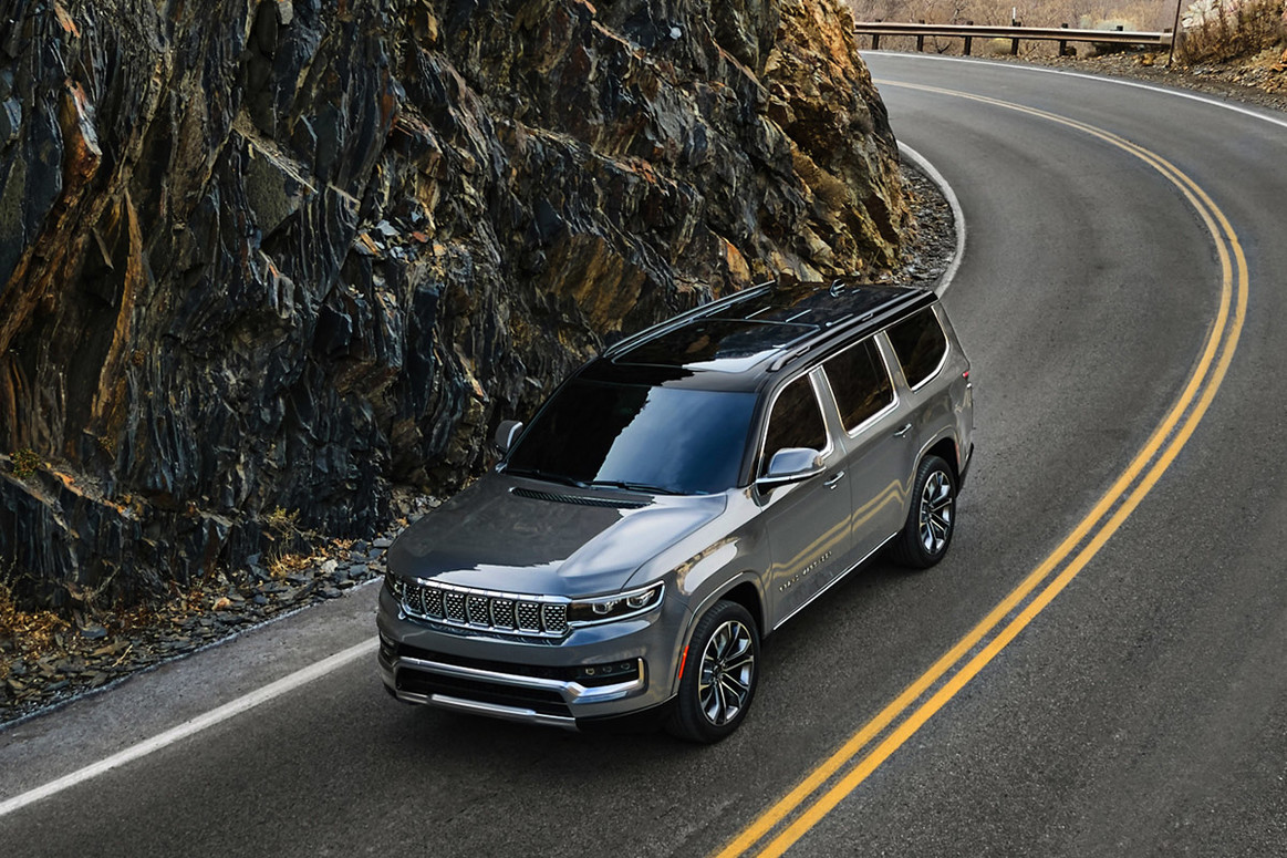 A silver All-New 2022 Grand Wagoneer being driven through a curved road through the mountains.