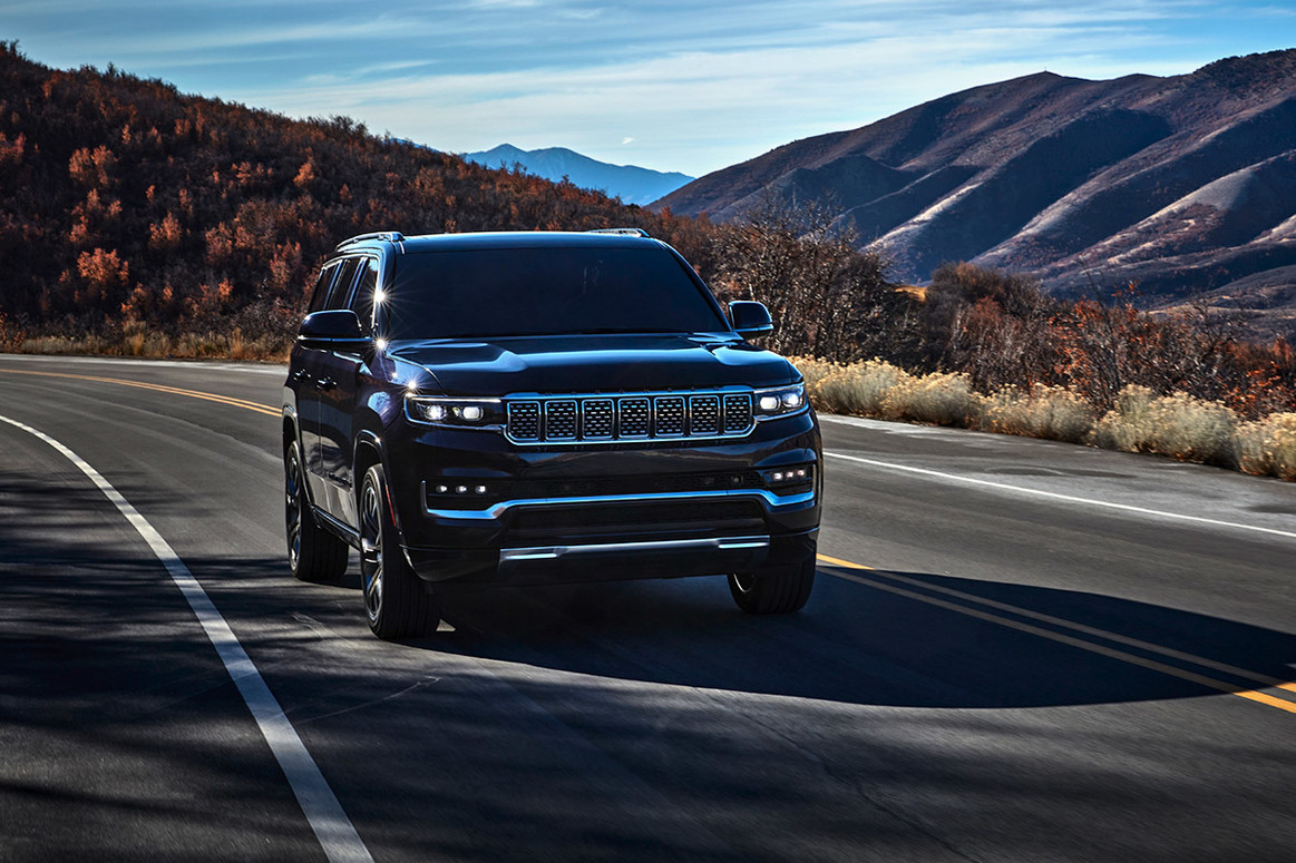 A black All-New 2022 Grand Wagoneer being driven on a paved road through the mountains.