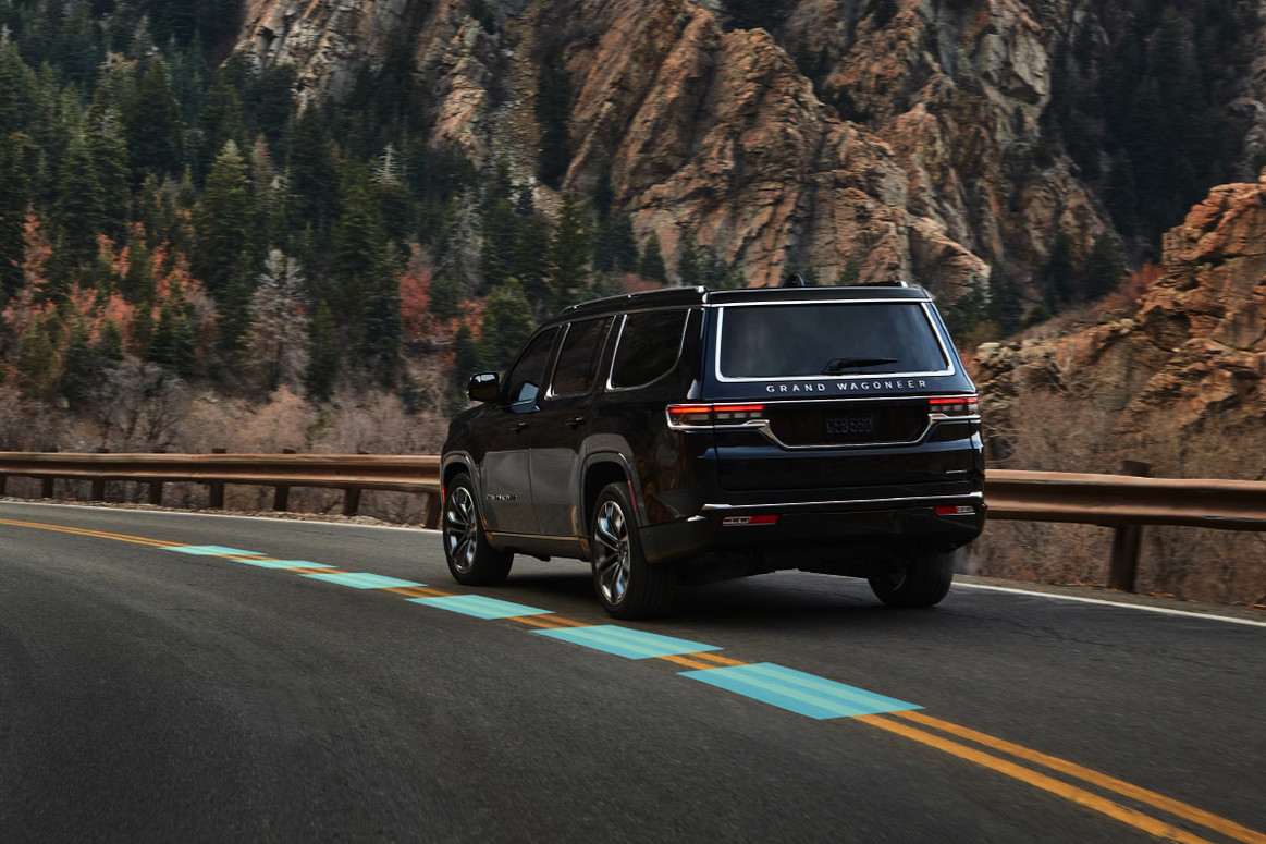 A black All-New 2022 Grand Wagoneer being driven through the mountains, with the yellow lines on the road highlighted to showcase the Active Driving Assist function.