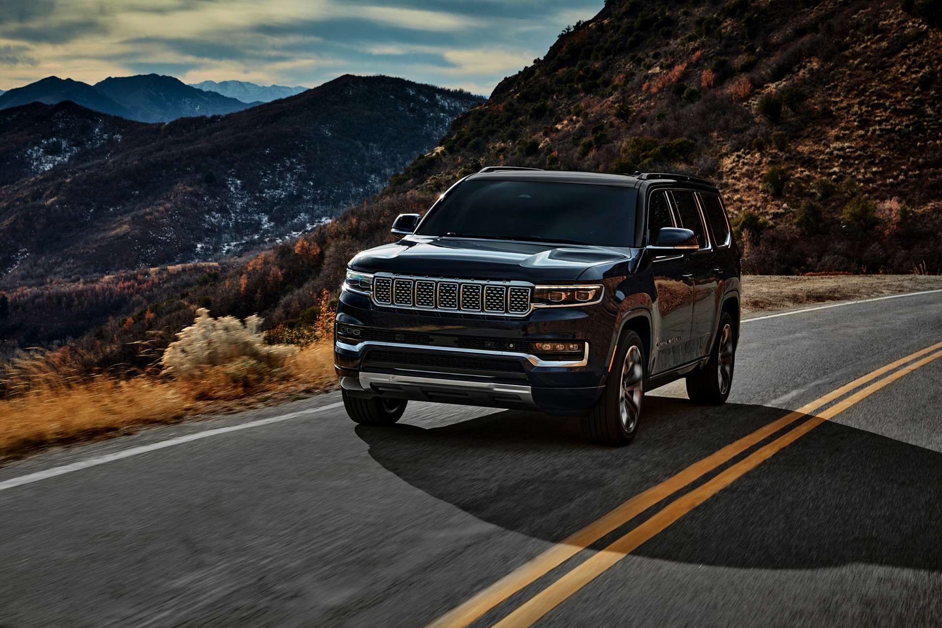 A black All-New 2022 Grand Wagoneer being driven on an open road through mountains.