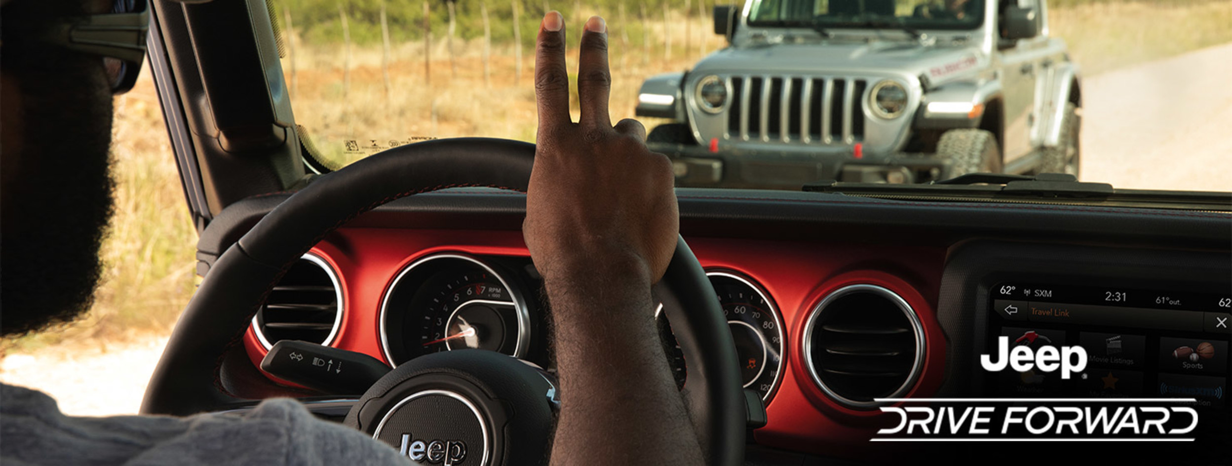 Jeep® Drive Forward. A driver in a Jeep® Wrangler driving down a dirt road, greeting another driver driving a grey Jeep® Wrangler on the other side of the road.