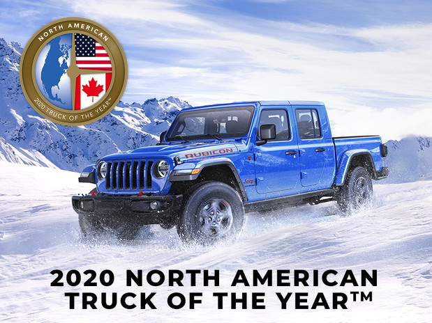 The blue all-new 2020 Jeep Gladiator Rubicon being driven on a snow-covered at a mountain during winter with NACTOY award logo.