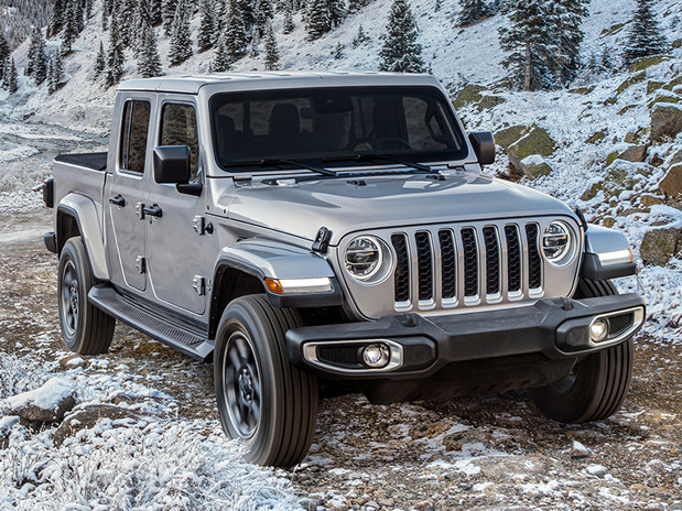 Jeep argent roulant hors route sur un sentier hivernal rocheux traversant des montagnes, le soleil se couchant en arrière-plan.