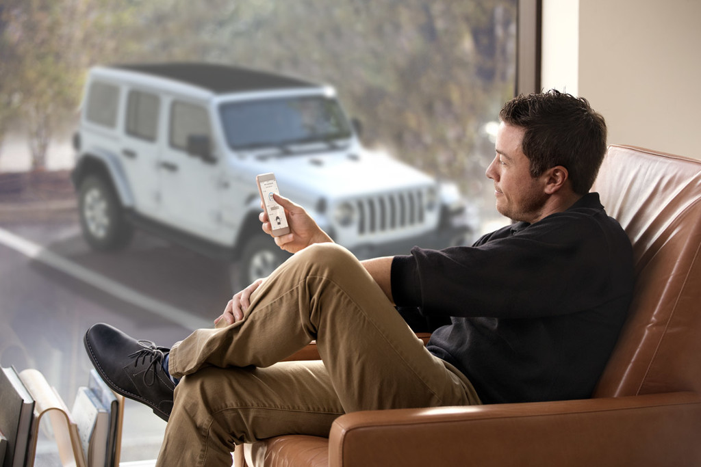 A person sitting and using their phone in front of a window with a white Jeep parked in the background.