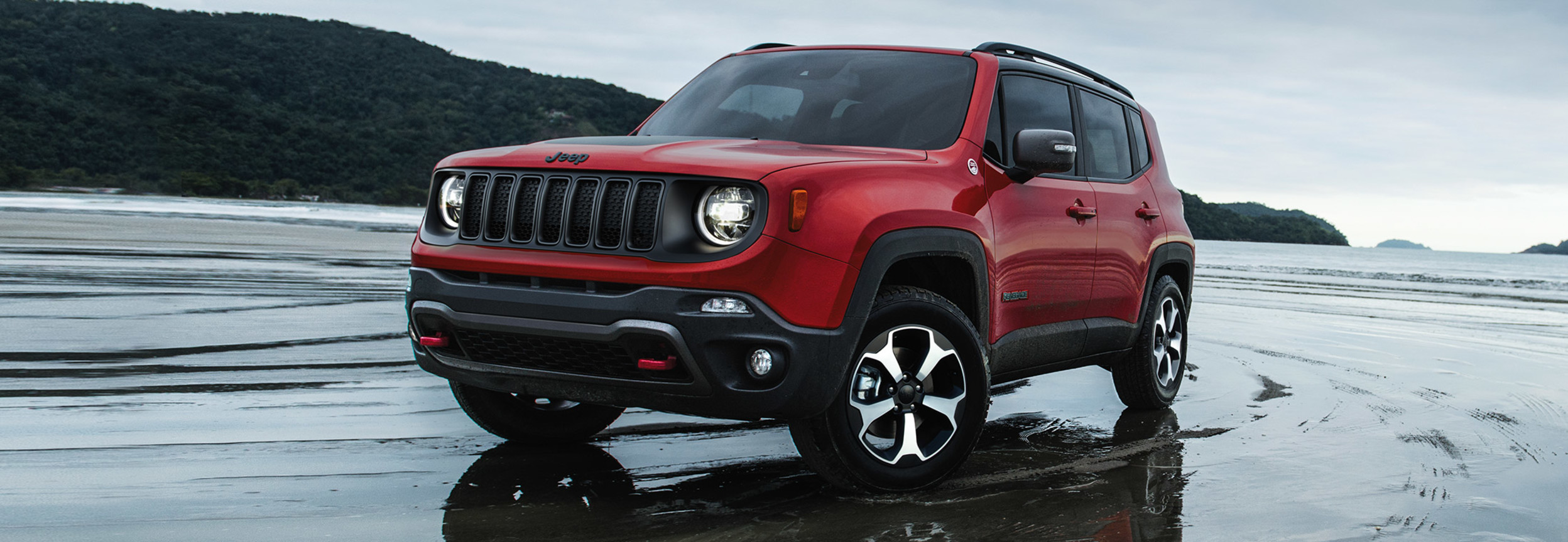 A red Jeep Renegade parked in the water on a beach