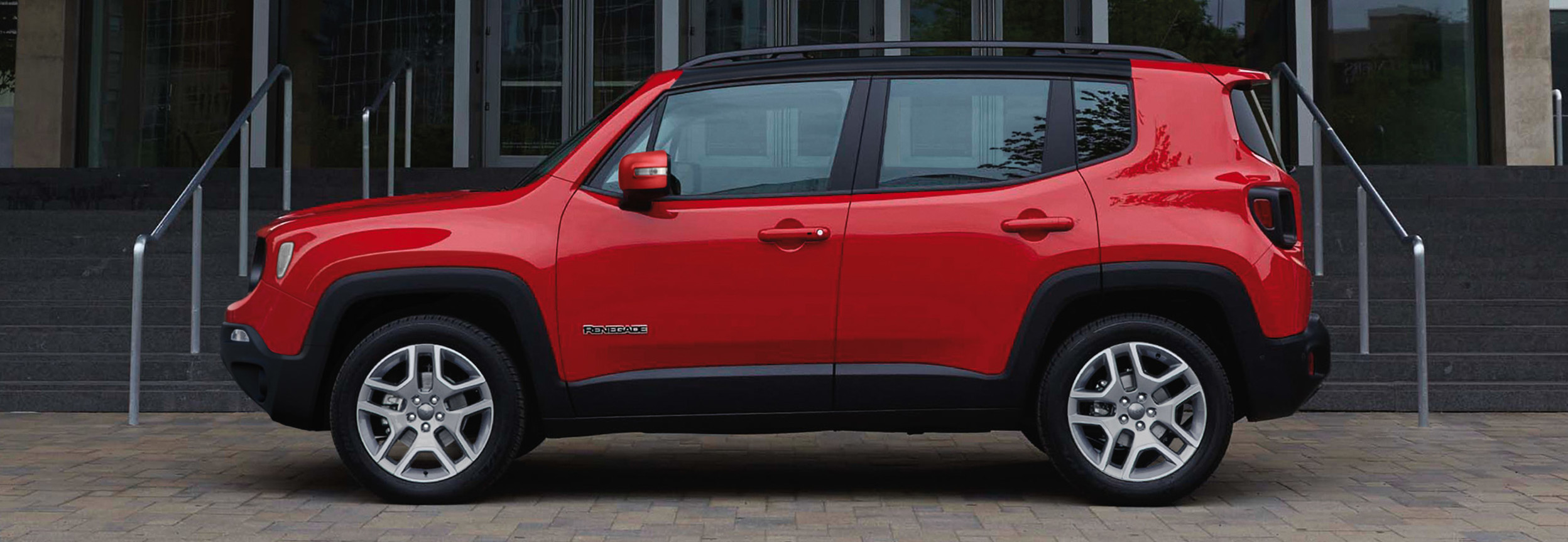 Side view of a red Jeep Renegade parked in front of a building